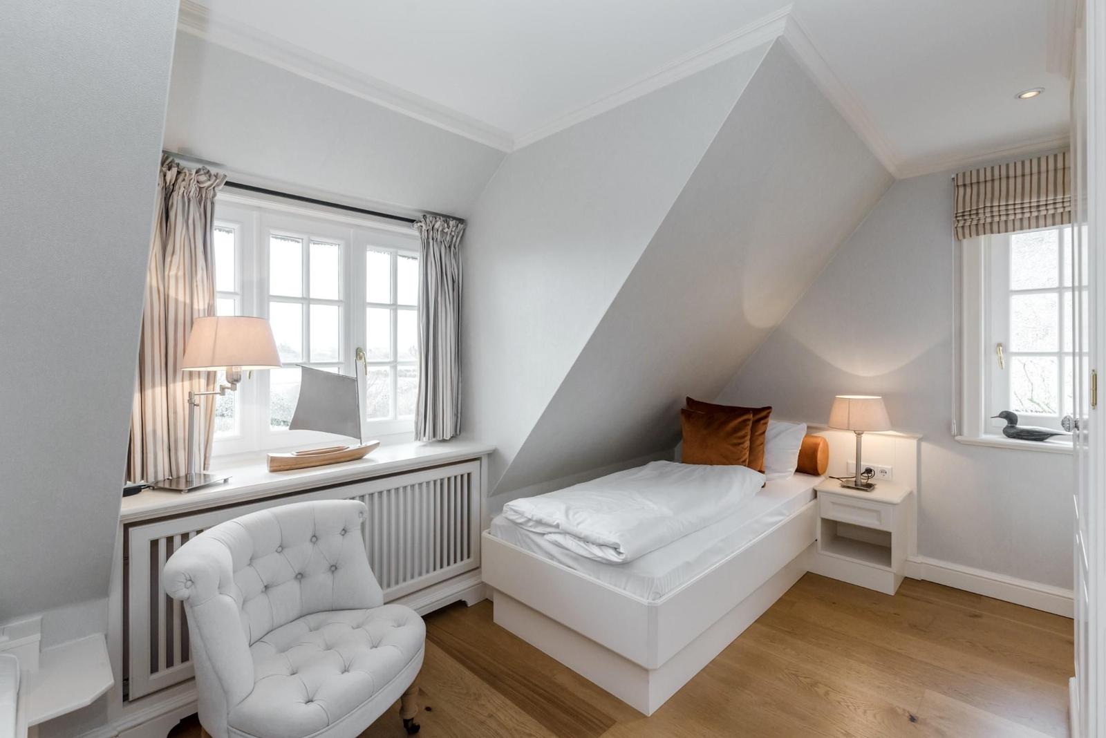Schlafzimmer mit Dachschrägen, weißem Bett und Stuhl an Fenster