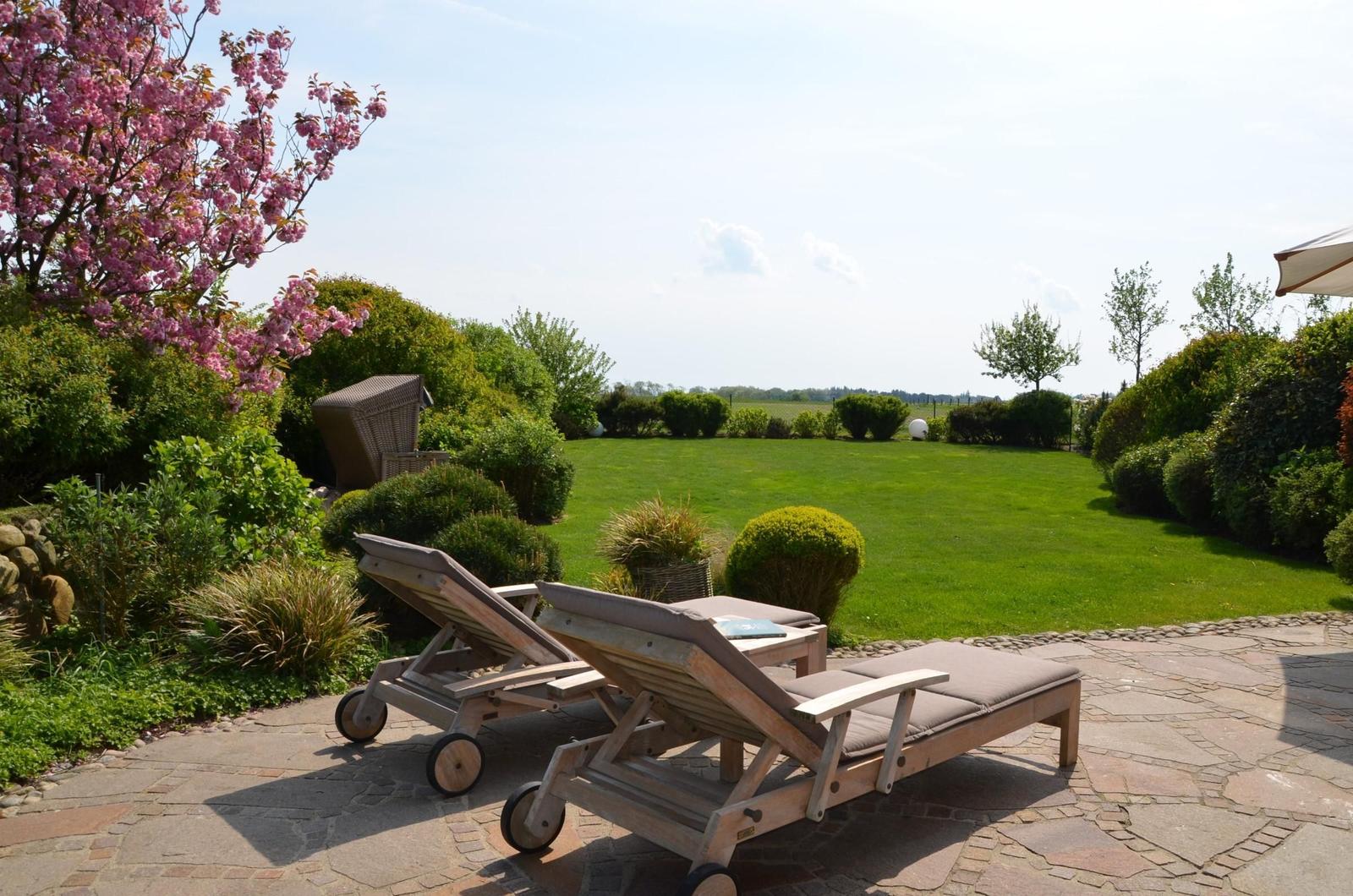 Zwei Liegestühle auf Steinplatten mit Blick auf grünen Rasen und blühenden Baum.