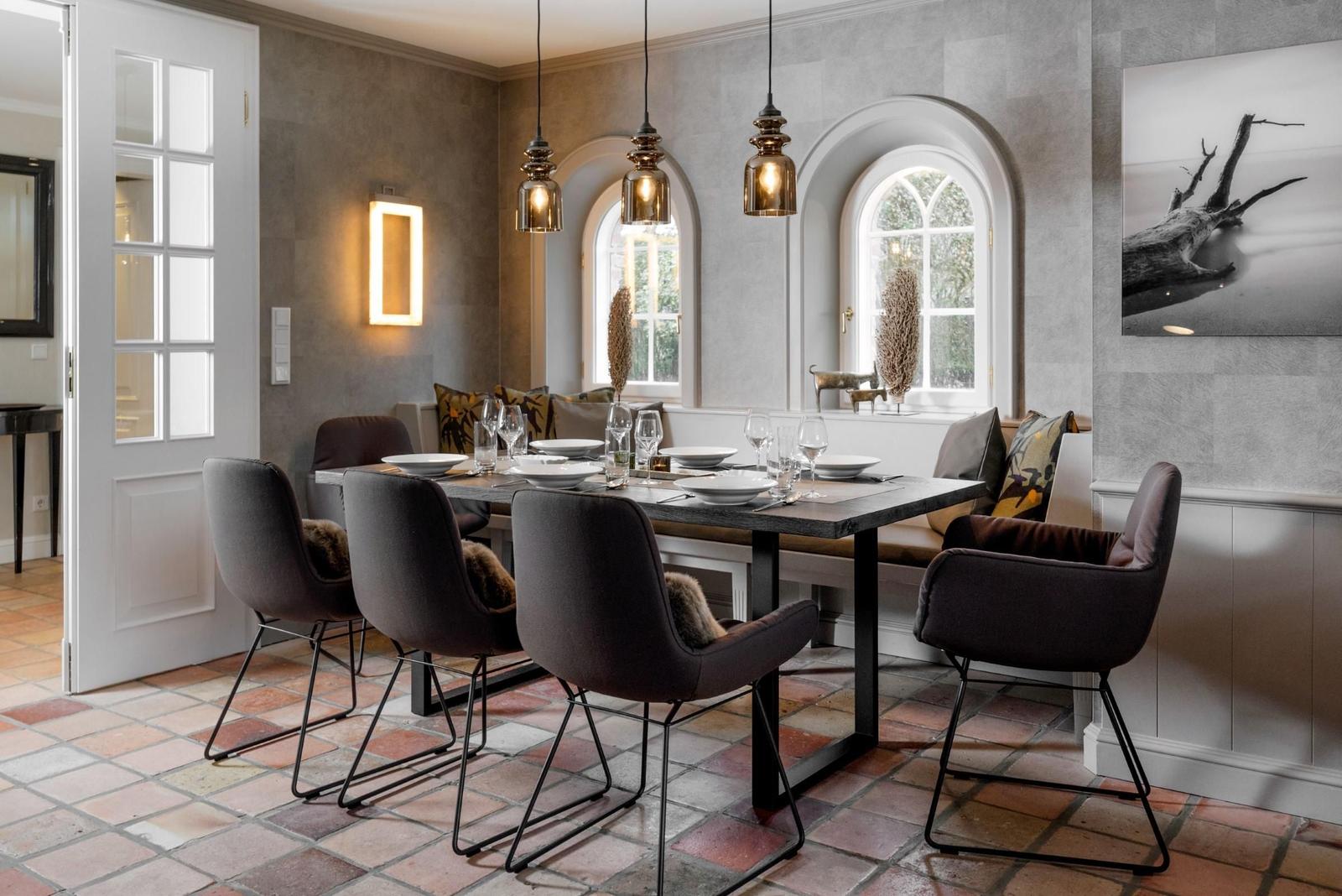 Esszimmer mit Tisch, Stühlen und Bänken unter Bogenfenstern.