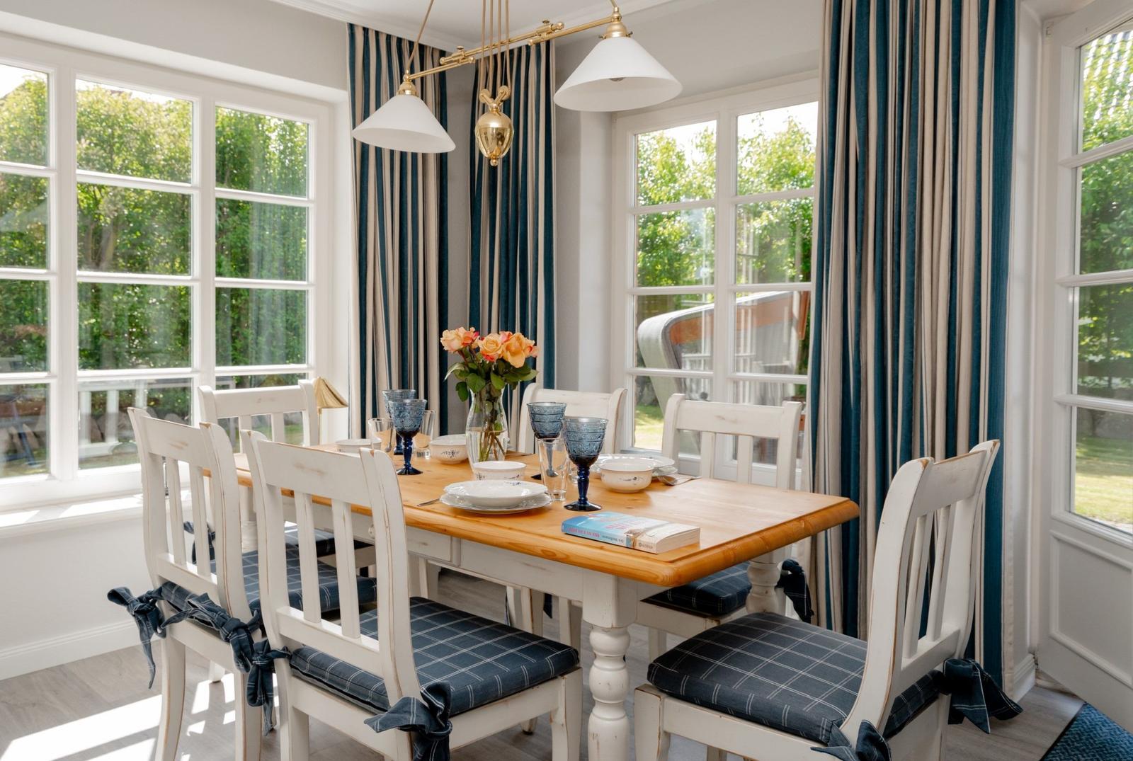 Esszimmer mit Holztisch, weißen Stühlen und blauen Gardinen.