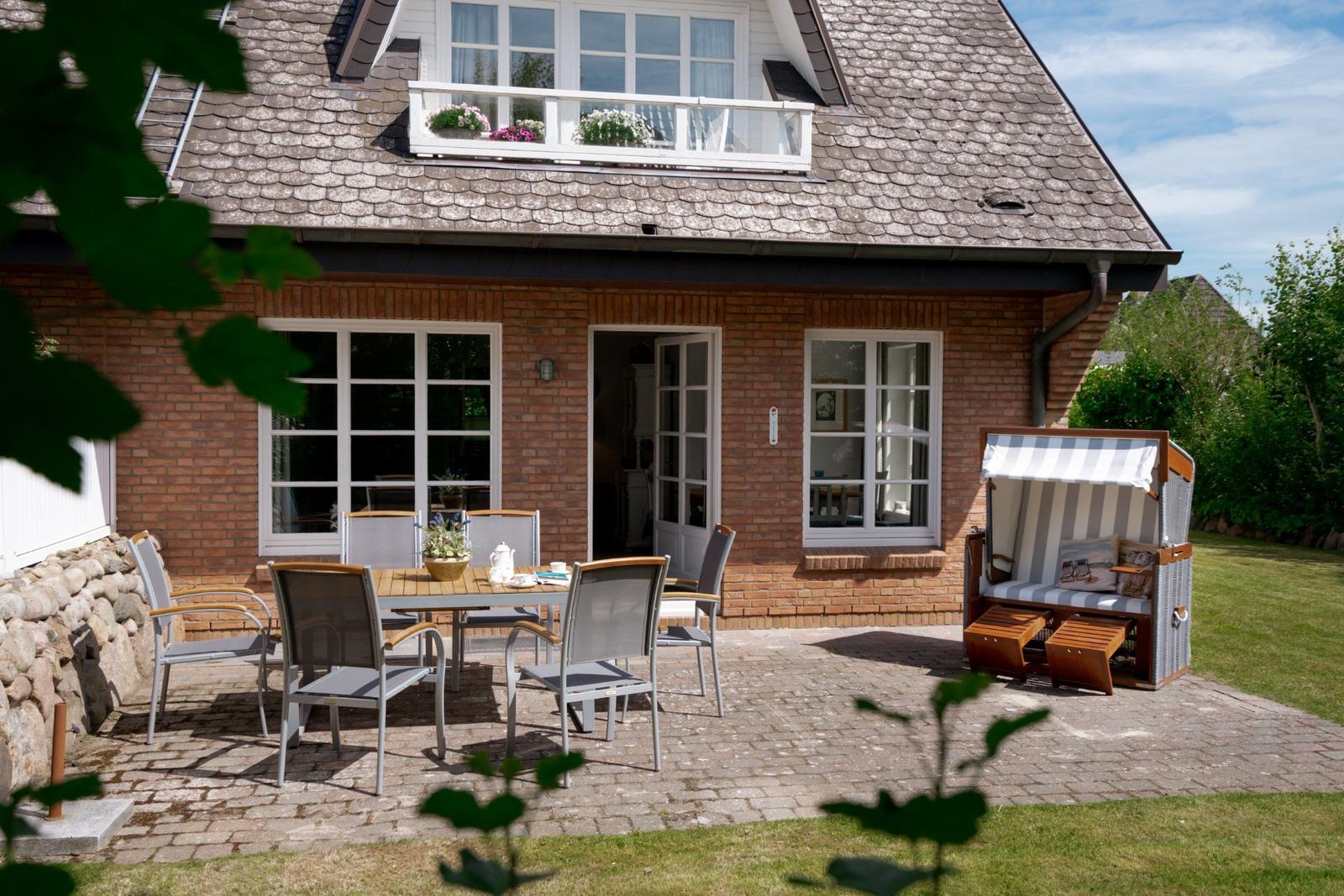 Haus mit Terrasse, Gartenmöbeln und Strandkorb.