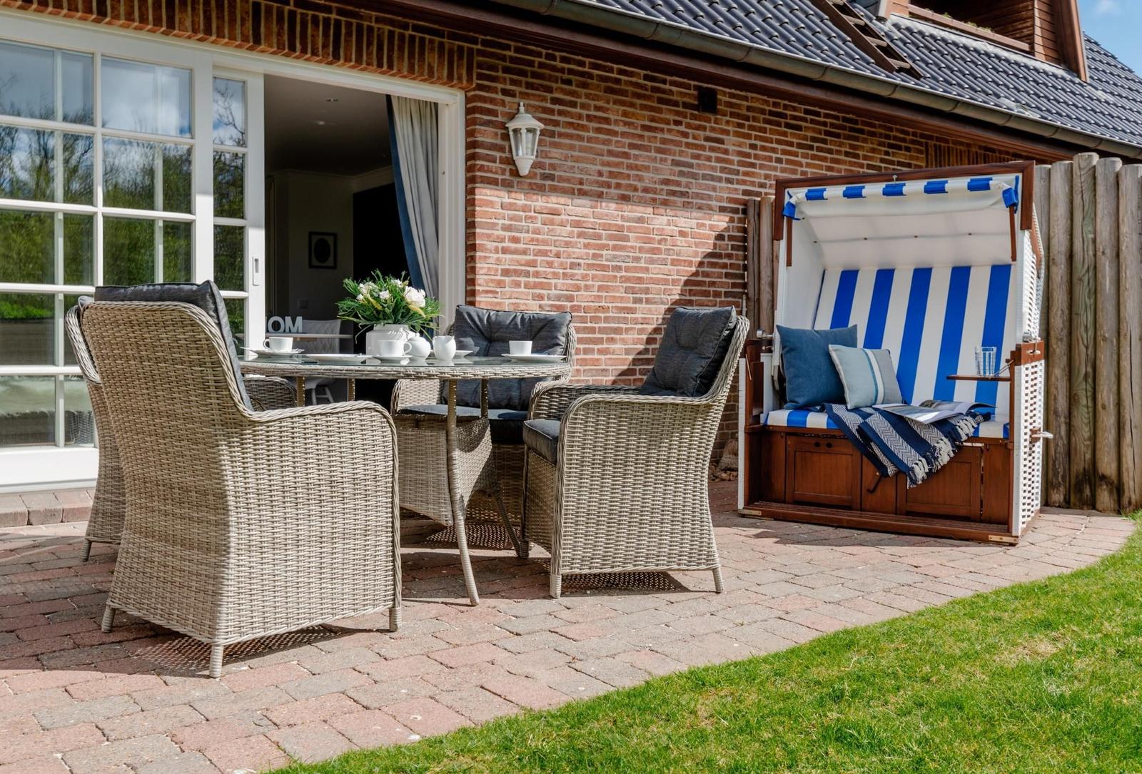 Terrasse mit Sitzgruppe und Strandkorb. Roter Kies und grüner Rasen.
