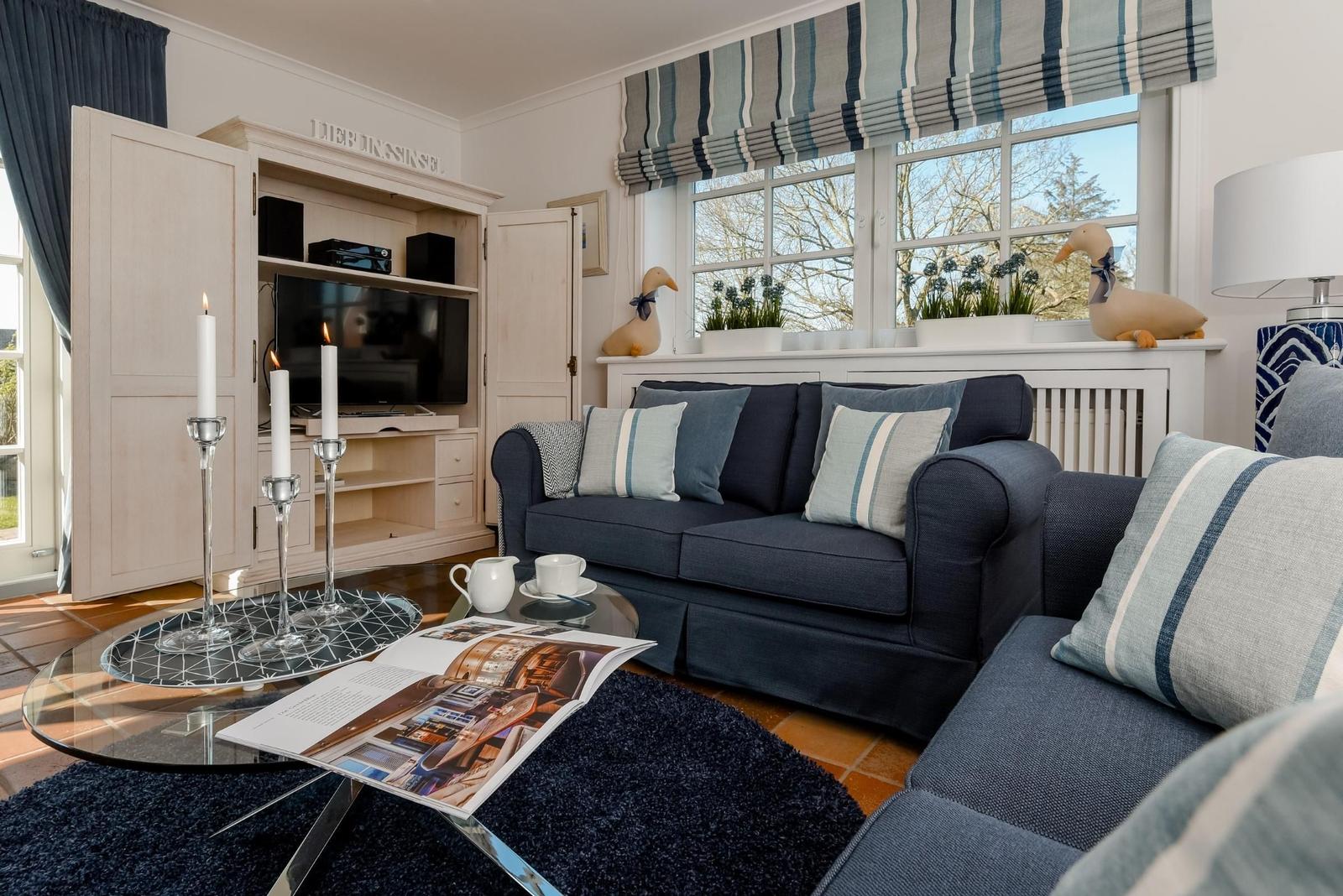 Ein Wohnzimmer mit Sofa, Fernseher und Fenster mit Blick auf den Garten.