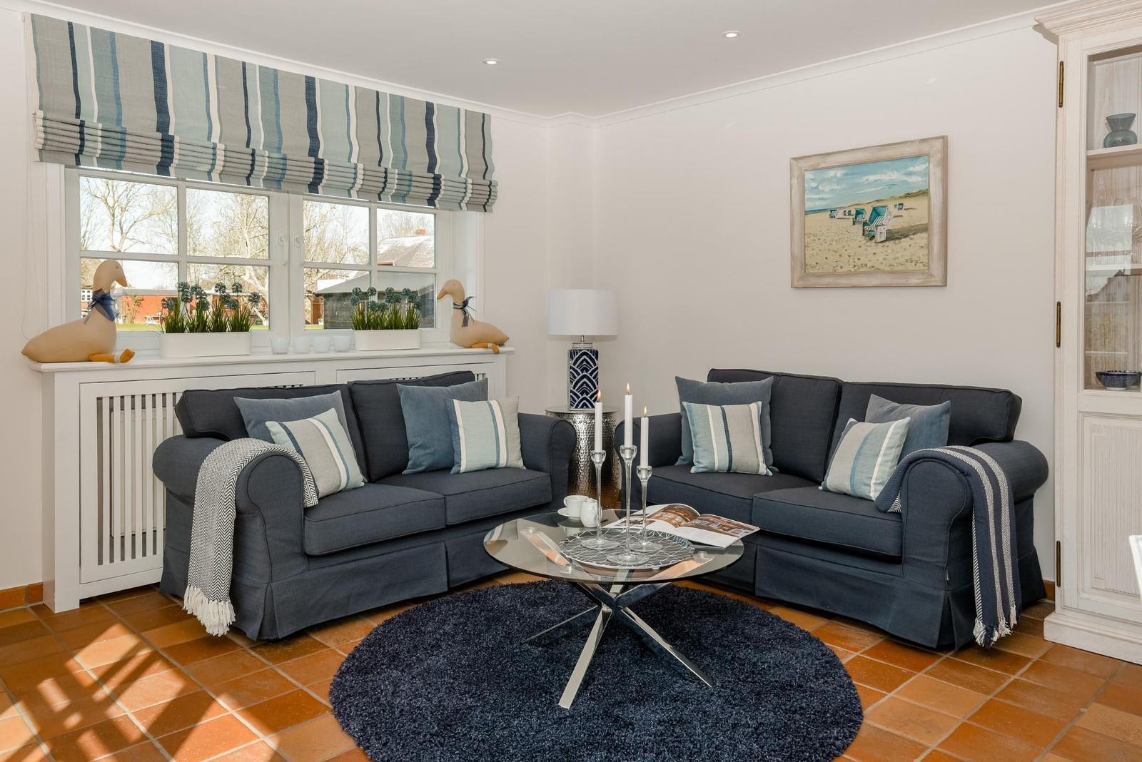 Ein Wohnzimmer mit zwei dunkelblauen Sofas, runden Teppich und Glas-Tisch.