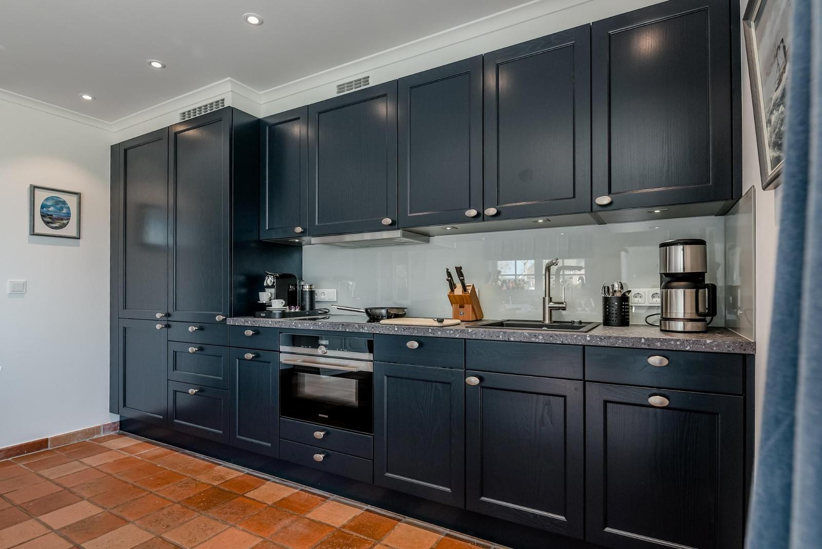 Küche mit dunklen Schränken, Edelstahlgeräten und Terrakottaboden.