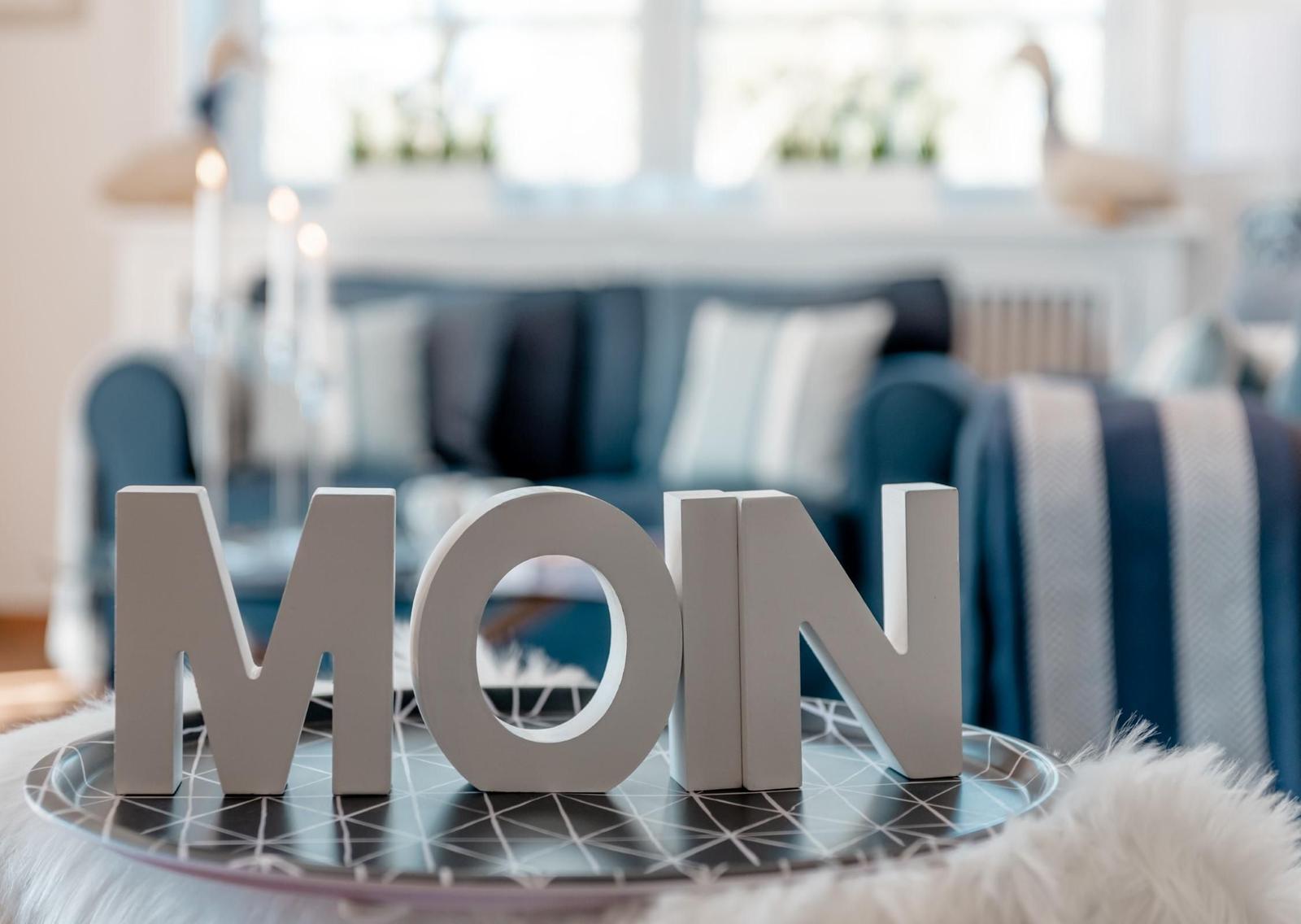 MOIN-Schriftzug auf Tisch, Sofa und Fenster im Hintergrund.
