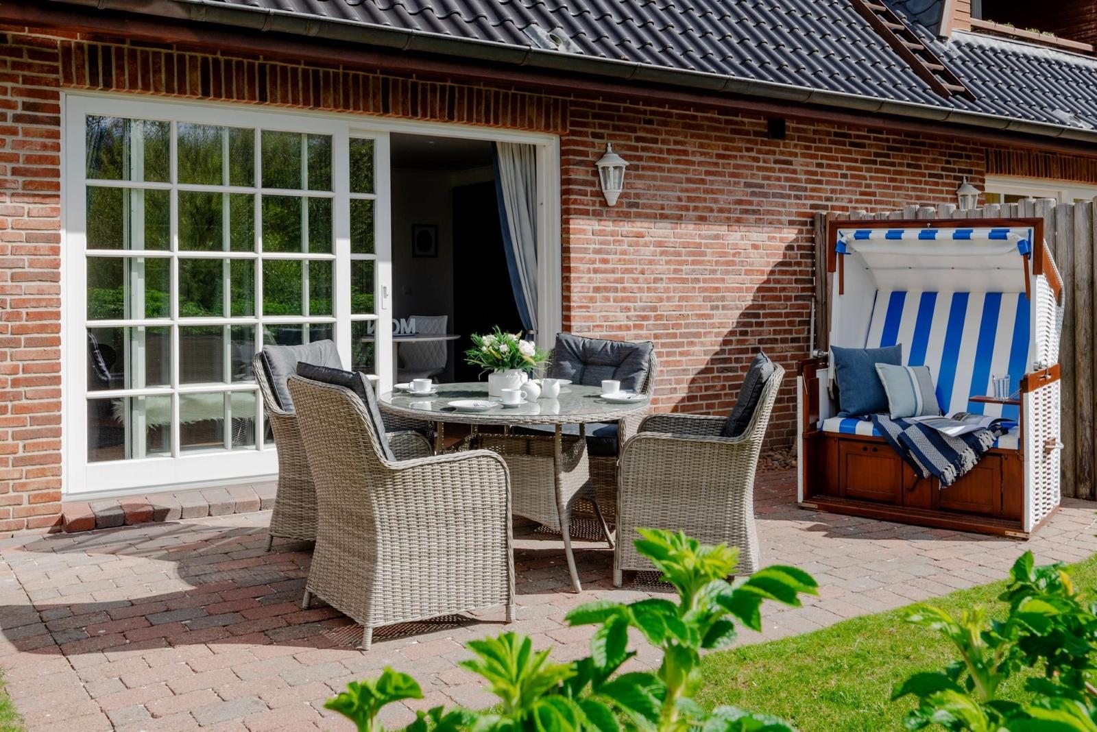 Terrasse mit Sitzgruppe, Strandkorb und Gartentisch. Blick ins Haus durch Fenster.