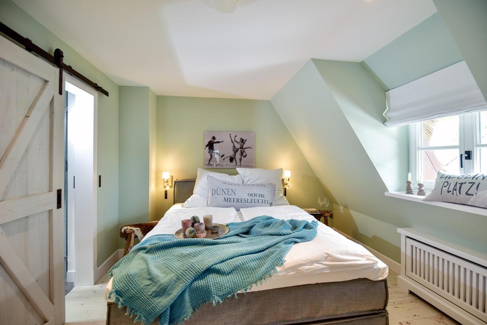 Schlafzimmer mit Dachschrägen, Bett, Fenster und Schiebetür.