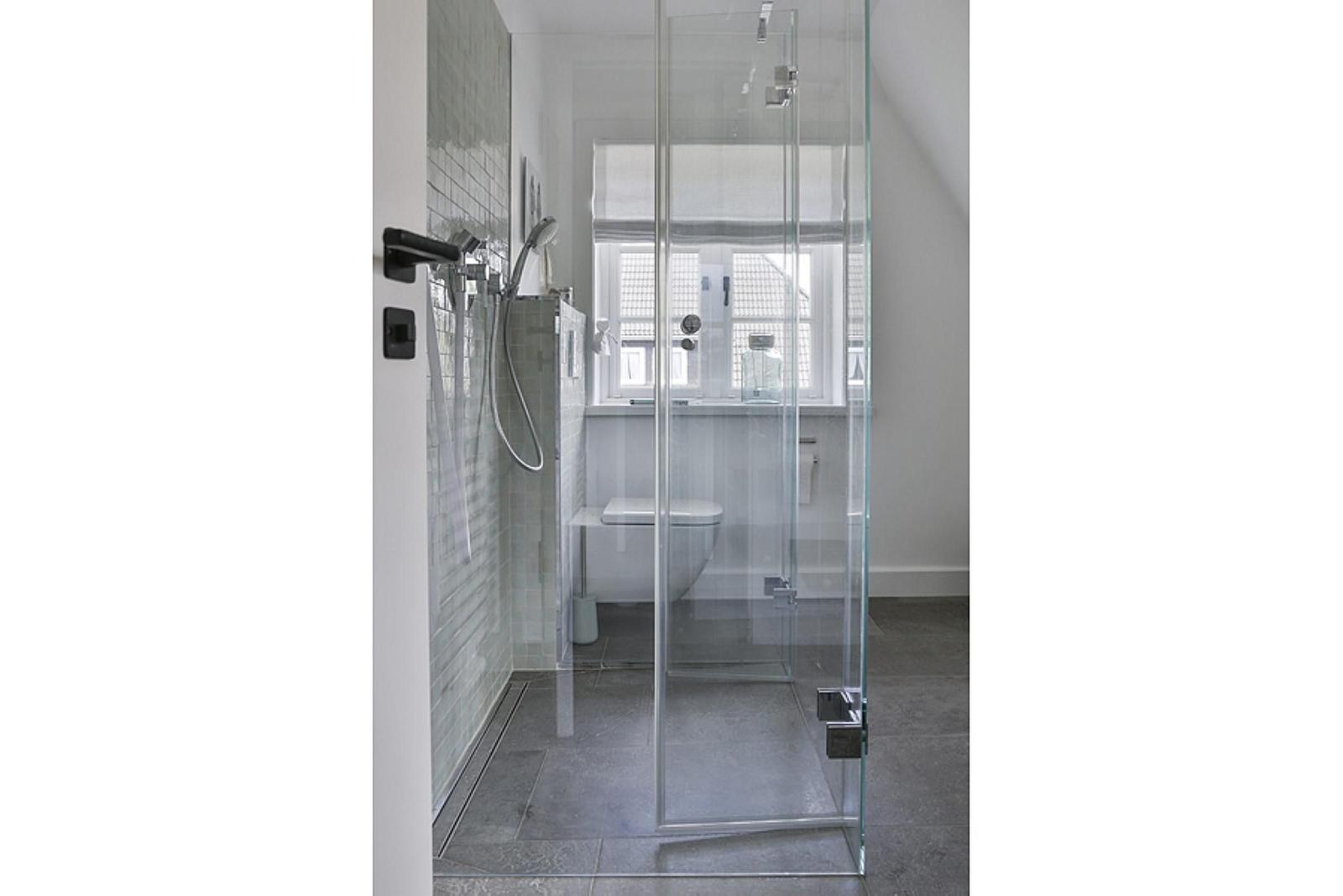 Duschbereich mit Glaswand, Toilette und Fenster im Badezimmer.