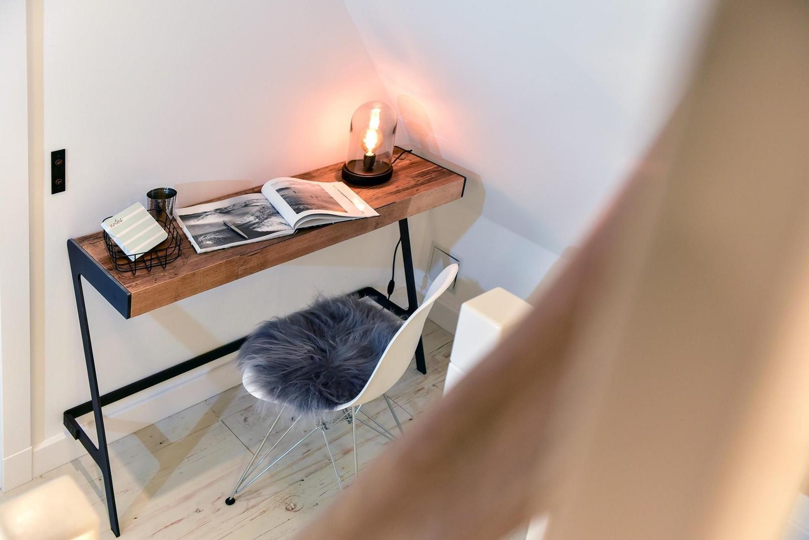 Schreibtisch mit Stuhl und Lampe in einem Raum mit schrägen Wänden.