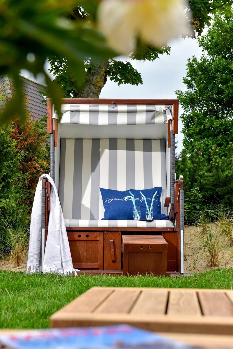 Hochwertiger Strandkorb mit blauem Kissen und Getränken im Garten.