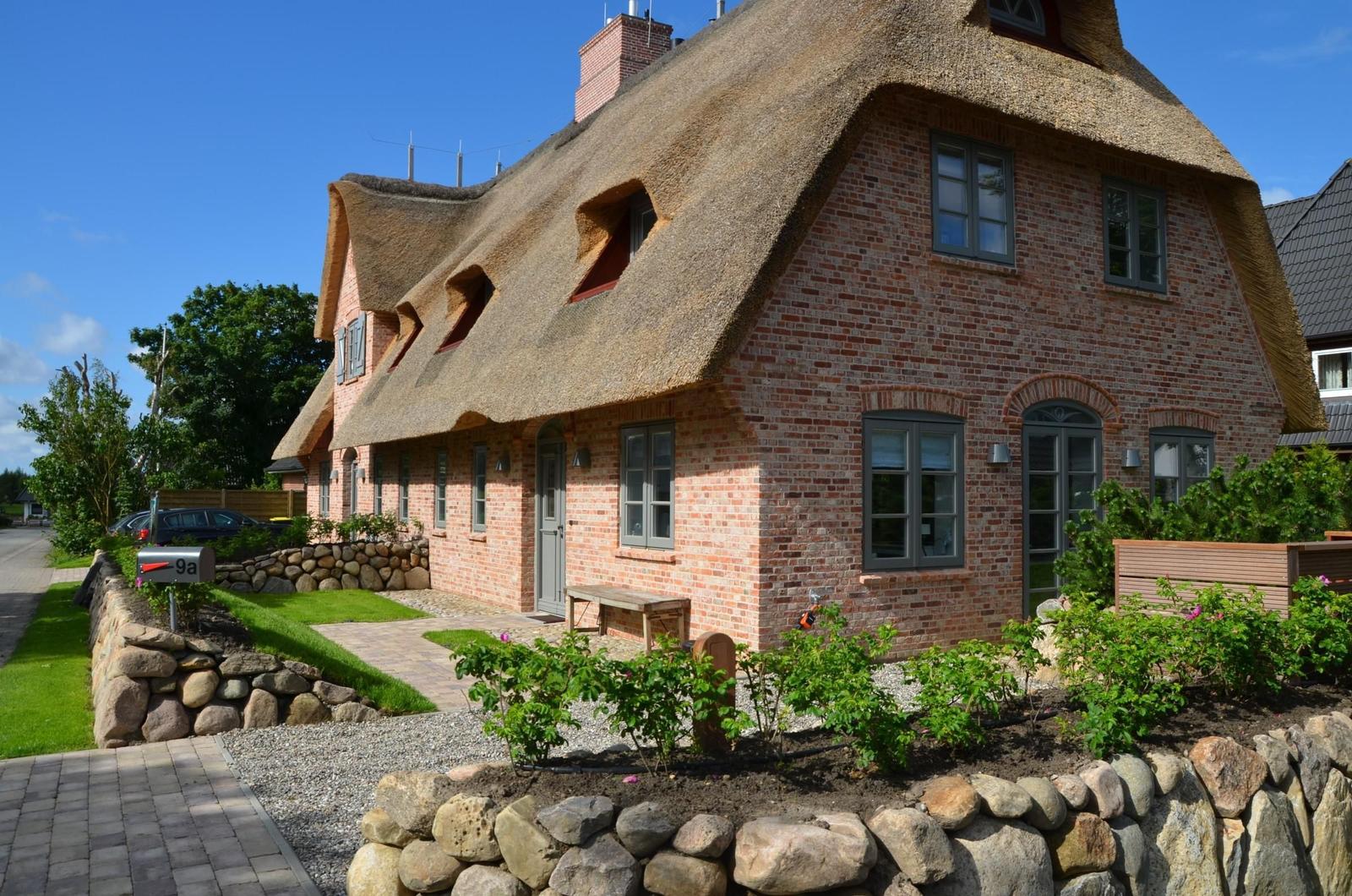 Rotes Backsteinhaus mit strohgedecktem Dach und grüner Umgebung.