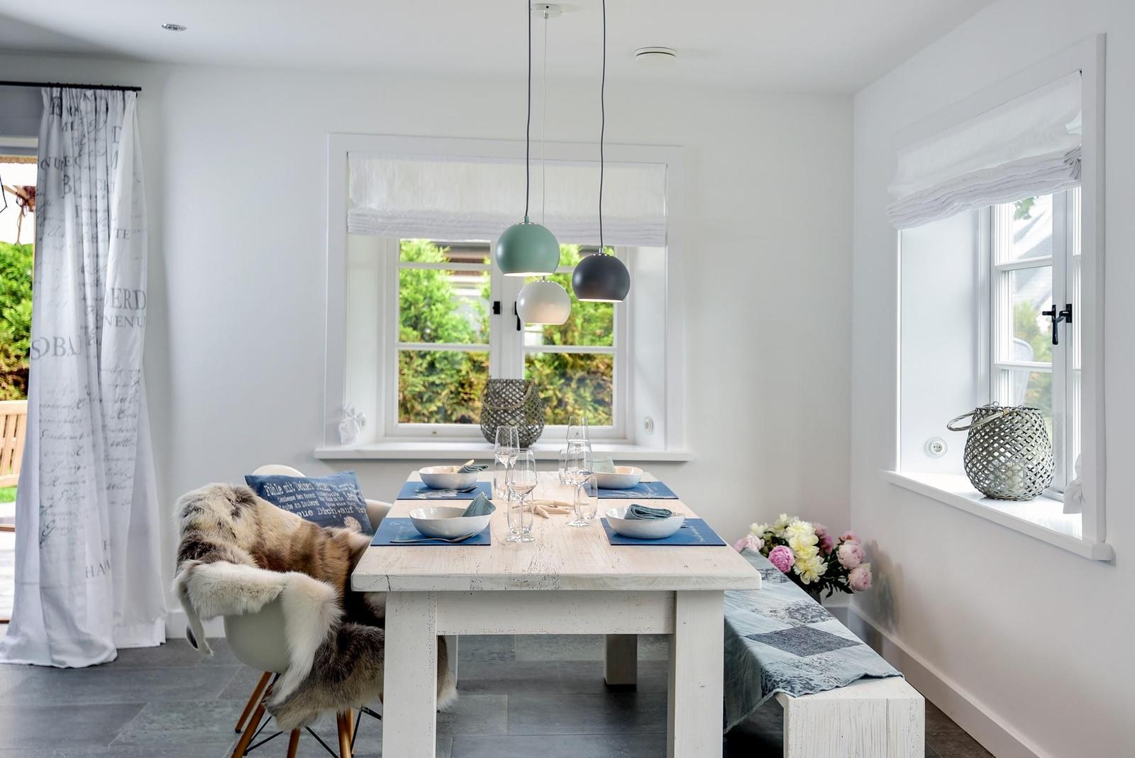 Esszimmer mit weißem Tisch, Stühlen und Fenstern. Blaue Tischdecken und Blumen auf dem Tisch.