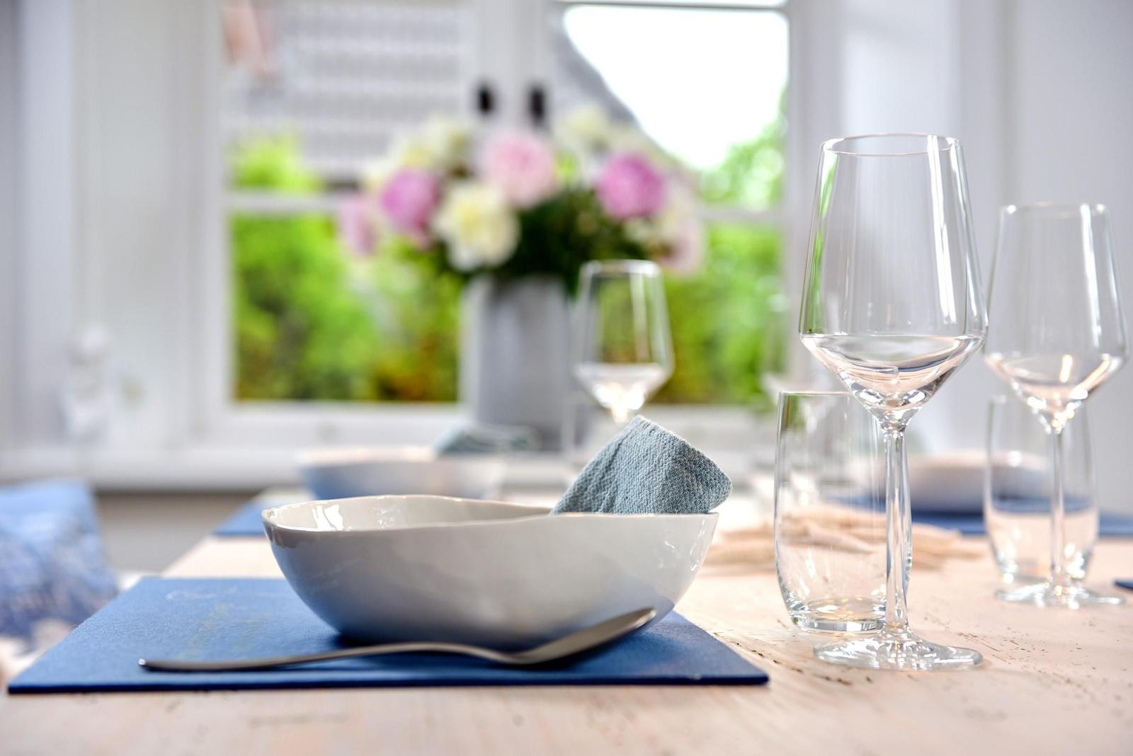 Tisch mit Teller, Gläsern und Blumenvase vor Fenster