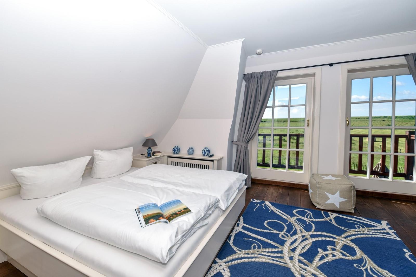 Schlafzimmer mit Doppelbett, Blick auf grünes Feld durch Fenster.