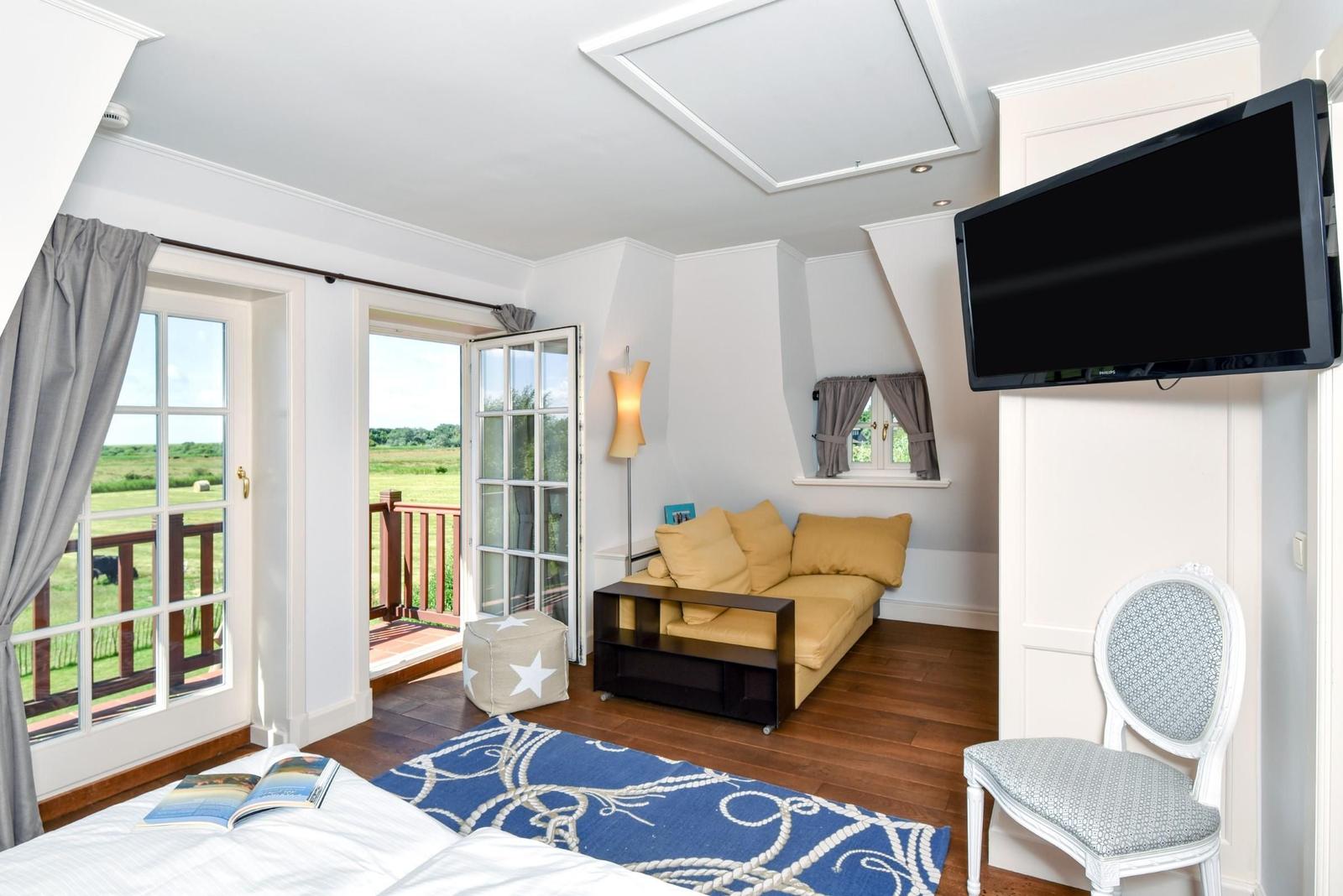 Schlafzimmer mit Sofa, Fernseher und Balkonblick auf grüne Landschaft.