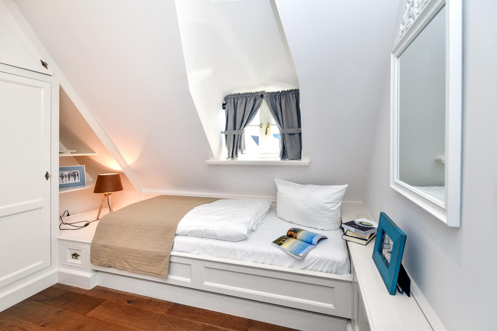 Schlafzimmer mit Dachschrägen, Bett, Fenster und Spiegel.