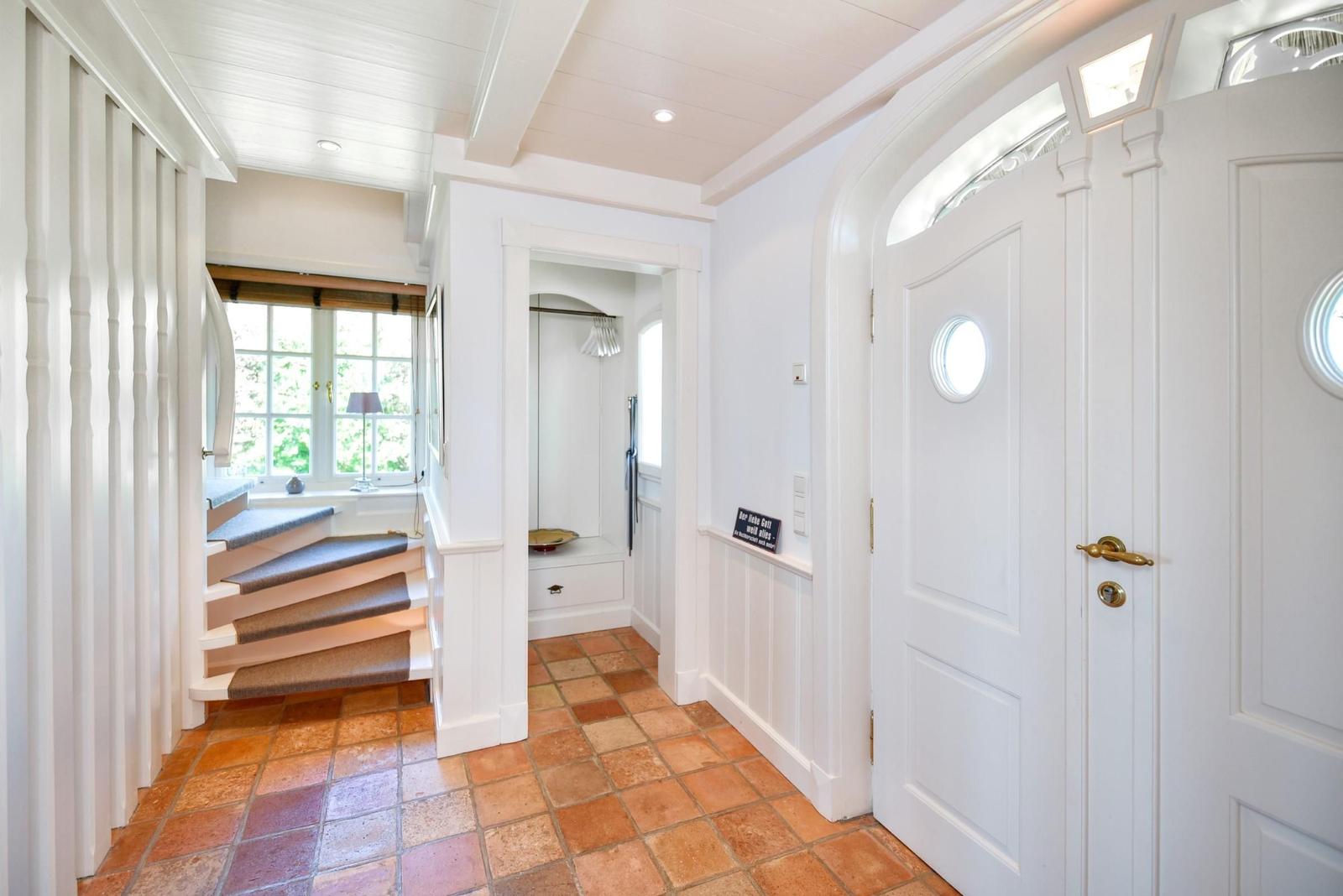 Haus mit Eingangstür, Flur und Treppe mit Holzstufen und Terrakottboden.