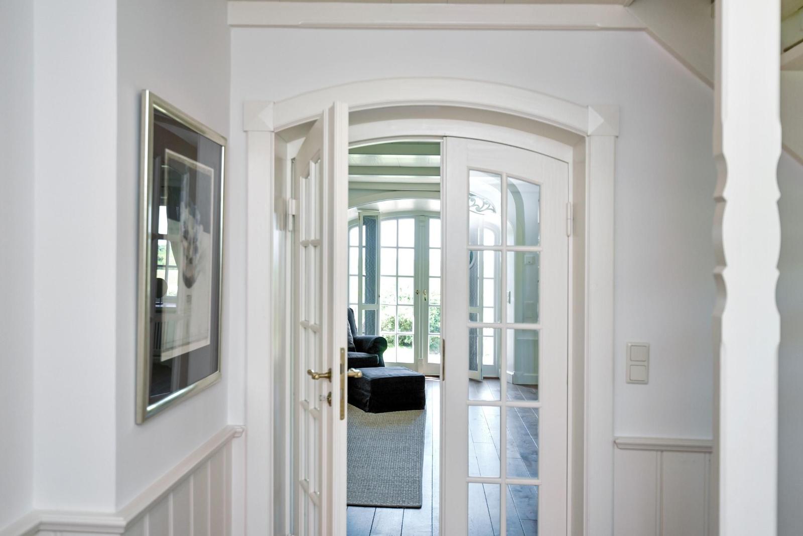 Durchgehend weißer Flur mit Tür zum Wohnbereich. Blick auf Sitzgelegenheit und Fenster.