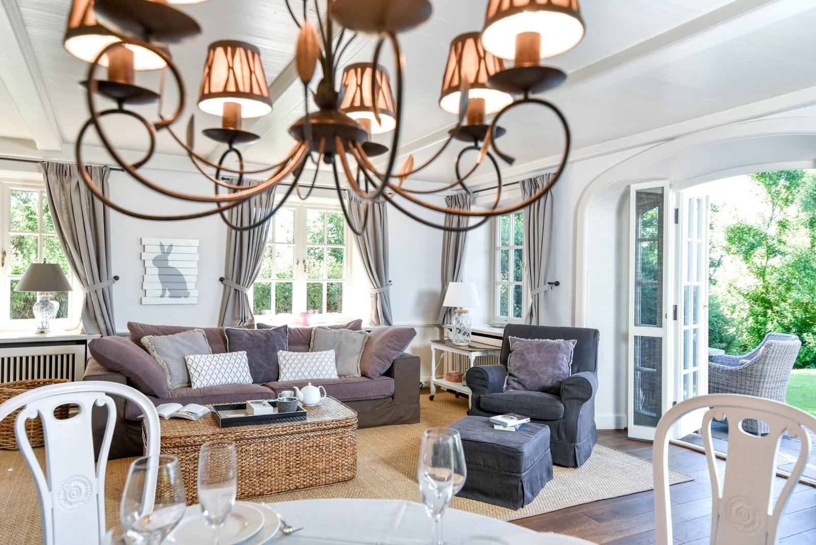 Wohn- und Essbereich mit Sofa, Stuhl und Kronleuchter. Durchgang zur Terrasse mit Garten.