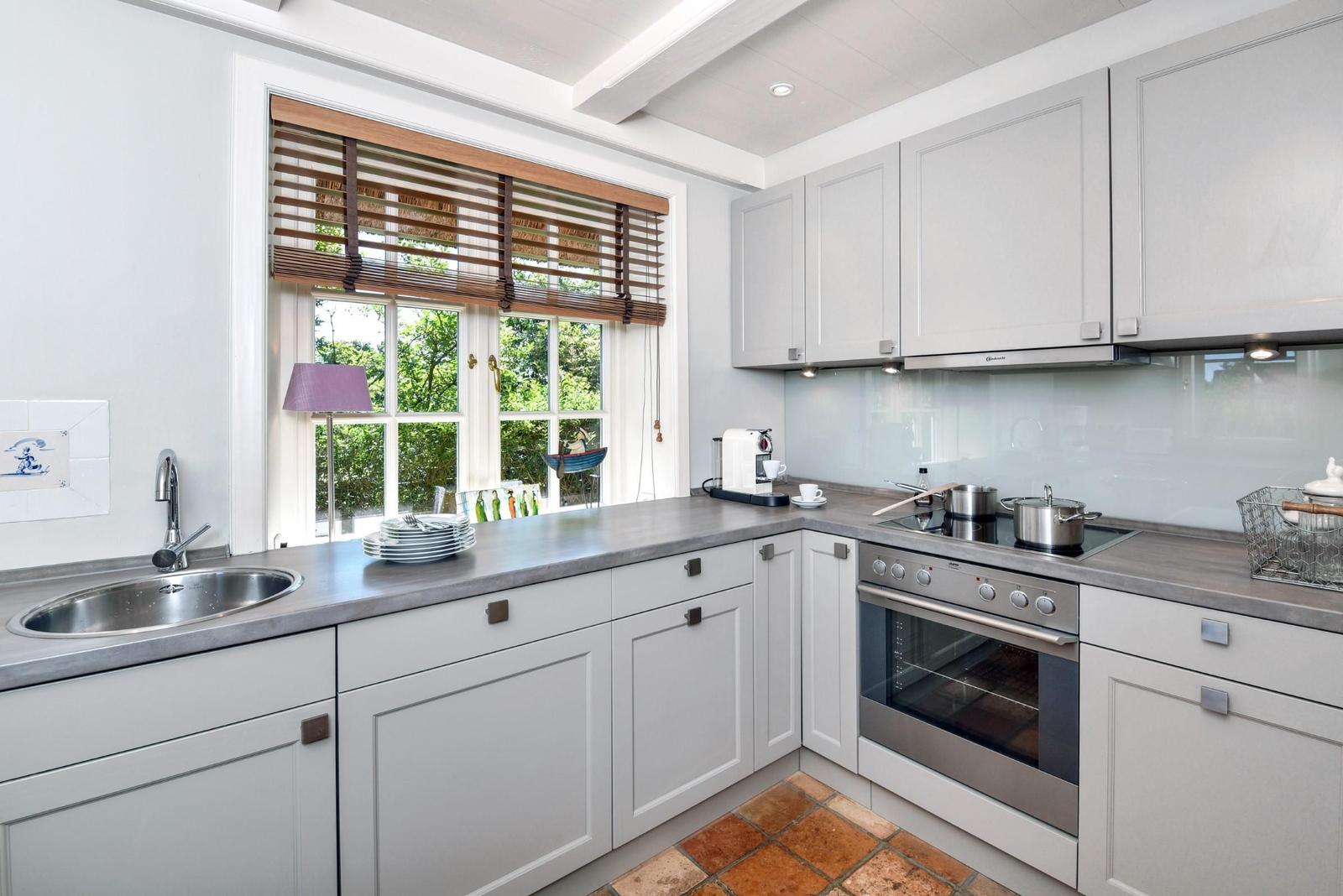 Küche mit hellen Schränken, Arbeitsplatte und Fenster mit Holzjalousie.