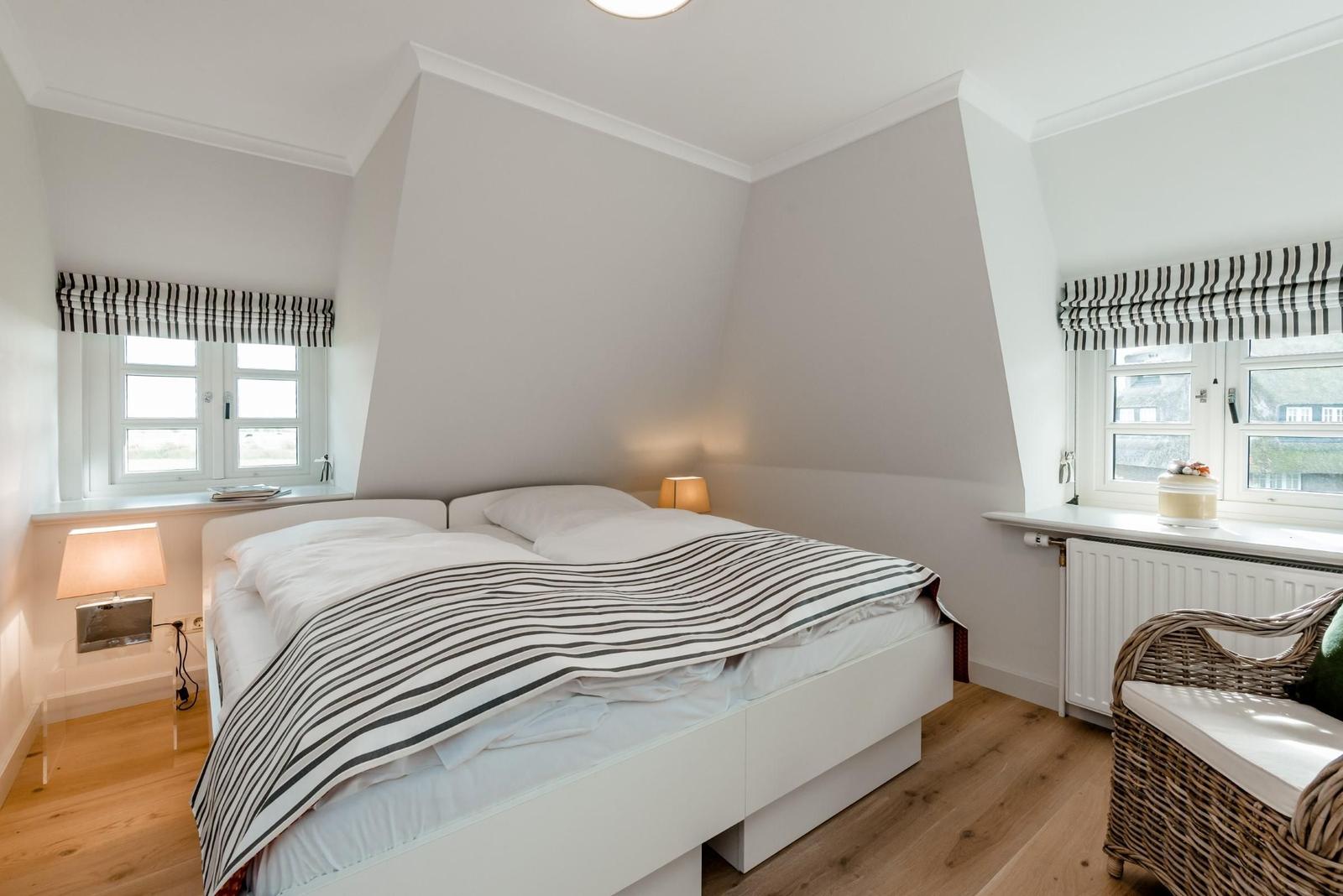 Bedroom with double bed, two windows, and wicker chair.