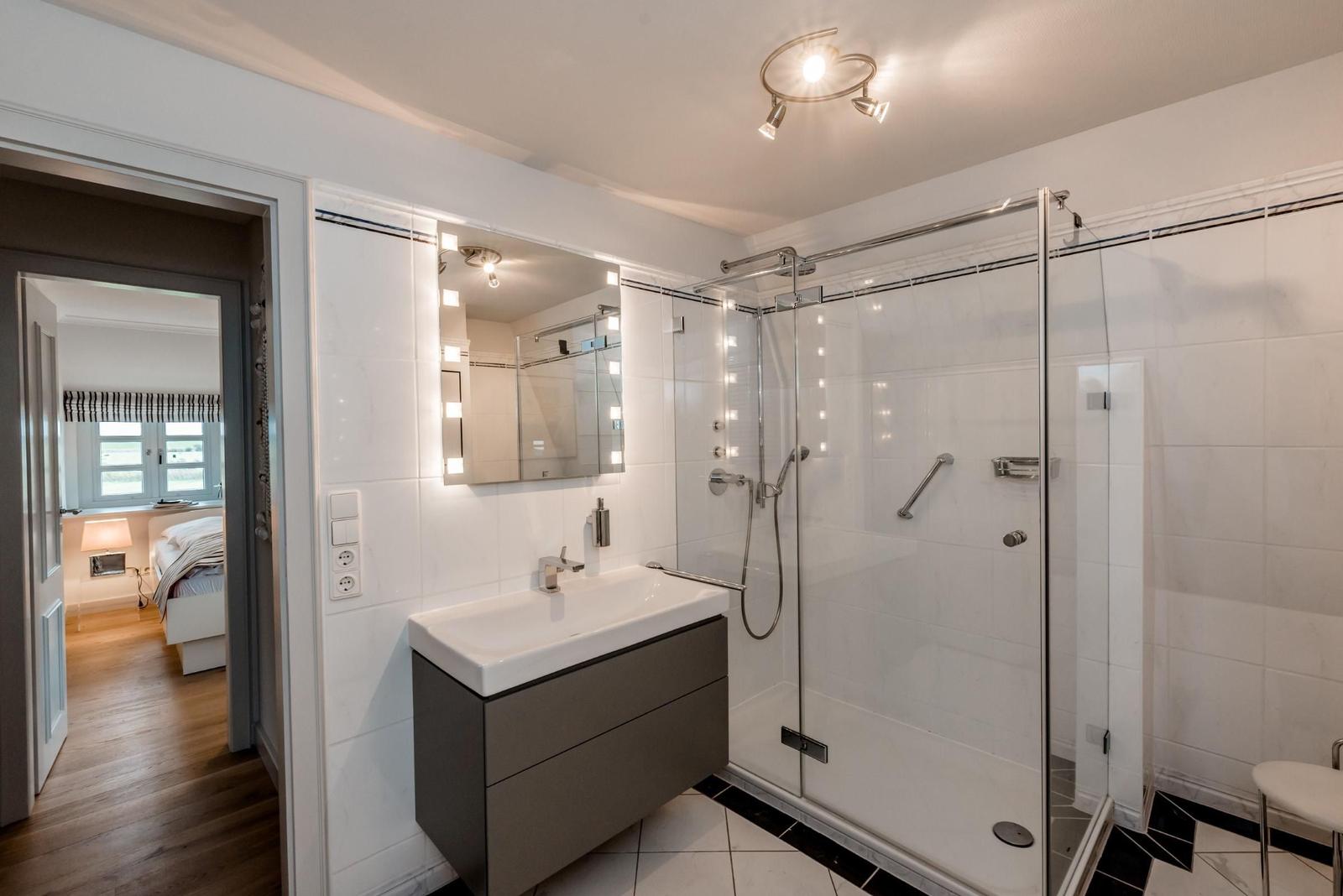 Bathroom with shower, sink, and mirror. Corridor to bedroom.