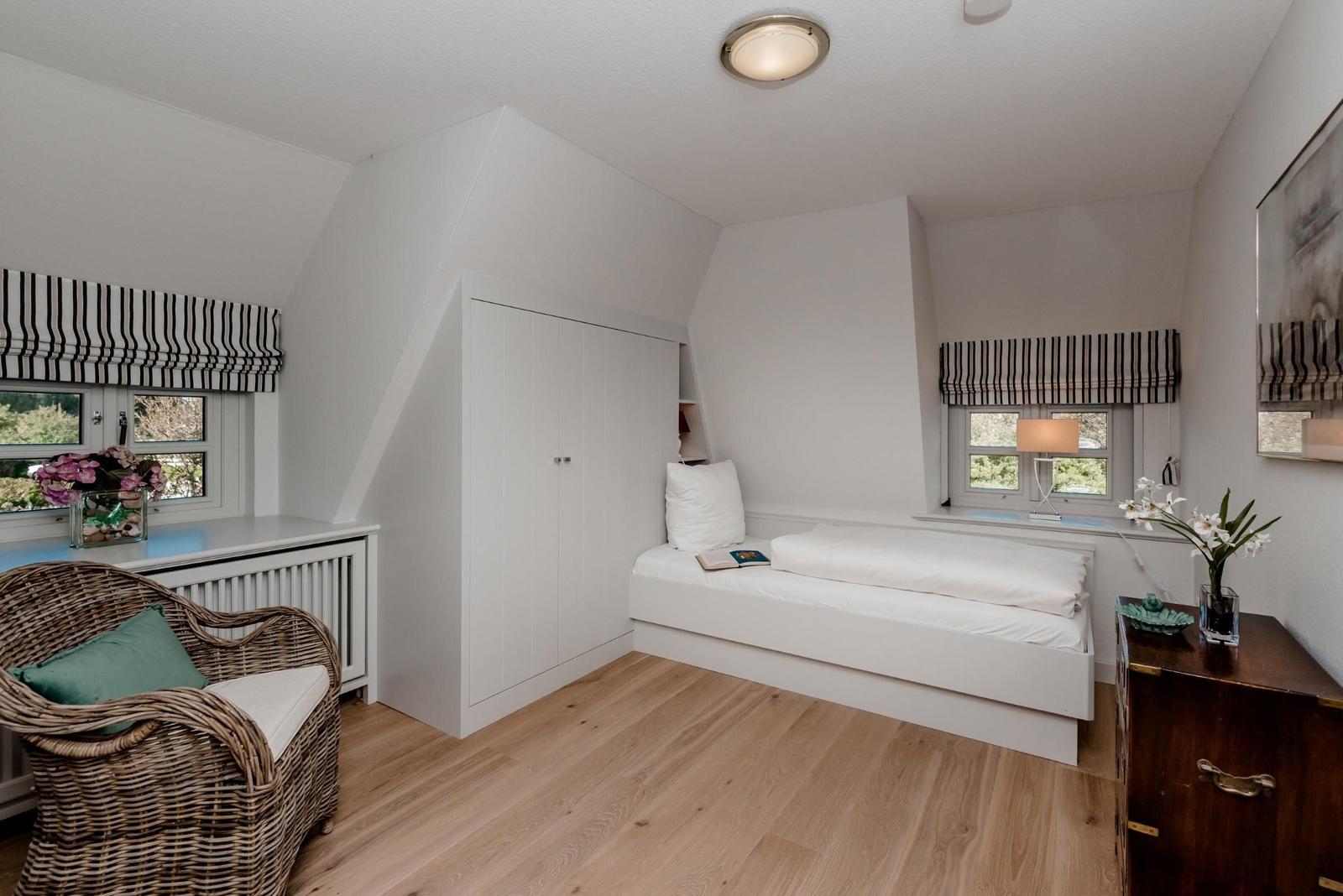 Bedroom with sloped ceiling, bed, wardrobe, and windows with blinds.