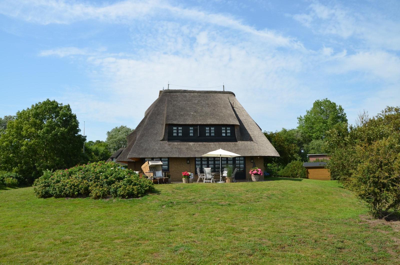 House with thatched roof, garden, terrace, and seating areas.