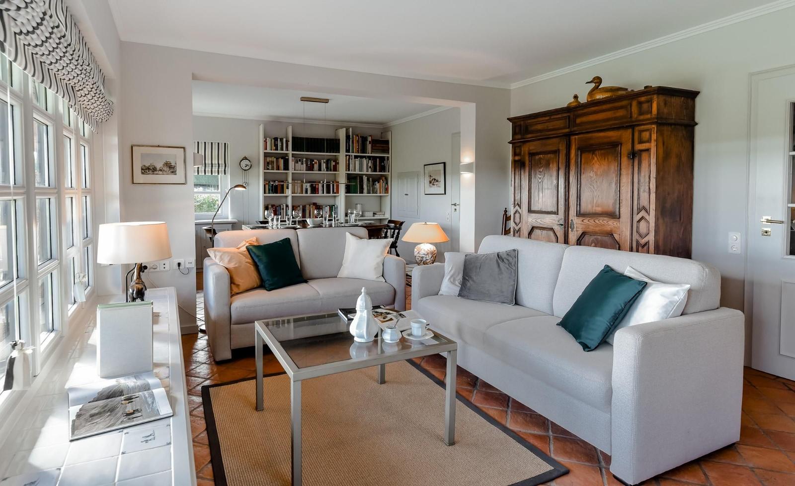Living room with two sofas, coffee table, and wooden cabinet. Passage to library with bookshelves.
