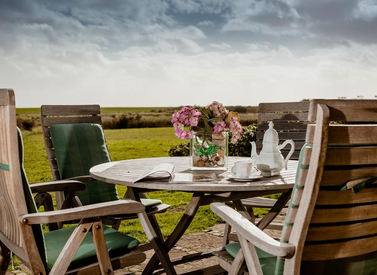 Wooden table with chairs, flowers, and tea service in the garden.
