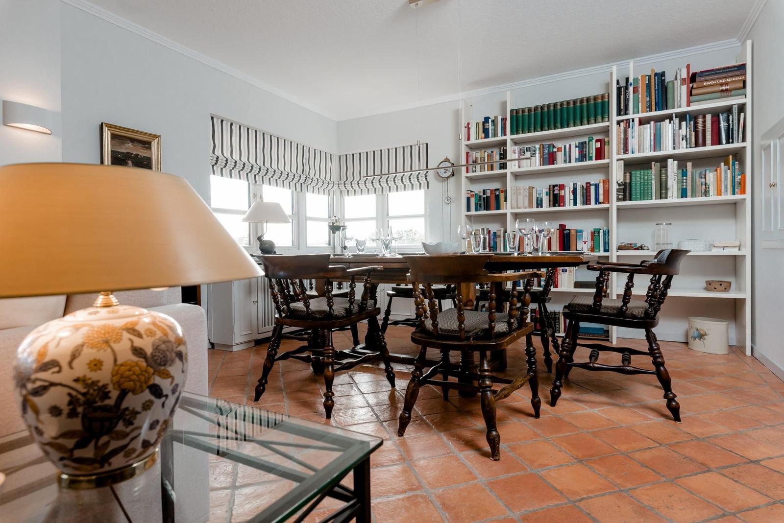 Dining room with wooden table, chairs, and bookshelf against the wall.