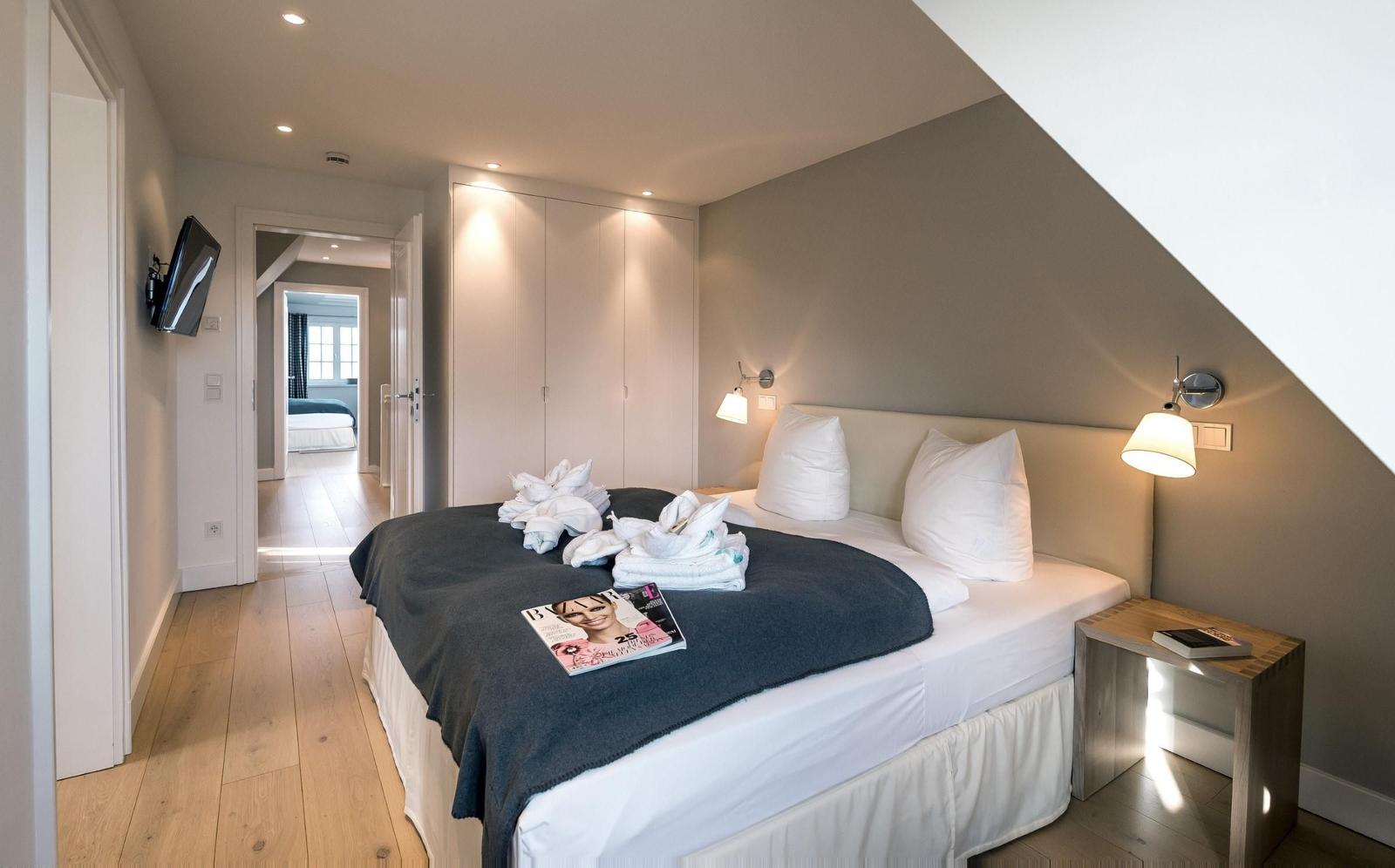 Schlafzimmer mit Doppelbett, Nachttisch, Wandlampen und Fernseher an der Wand.