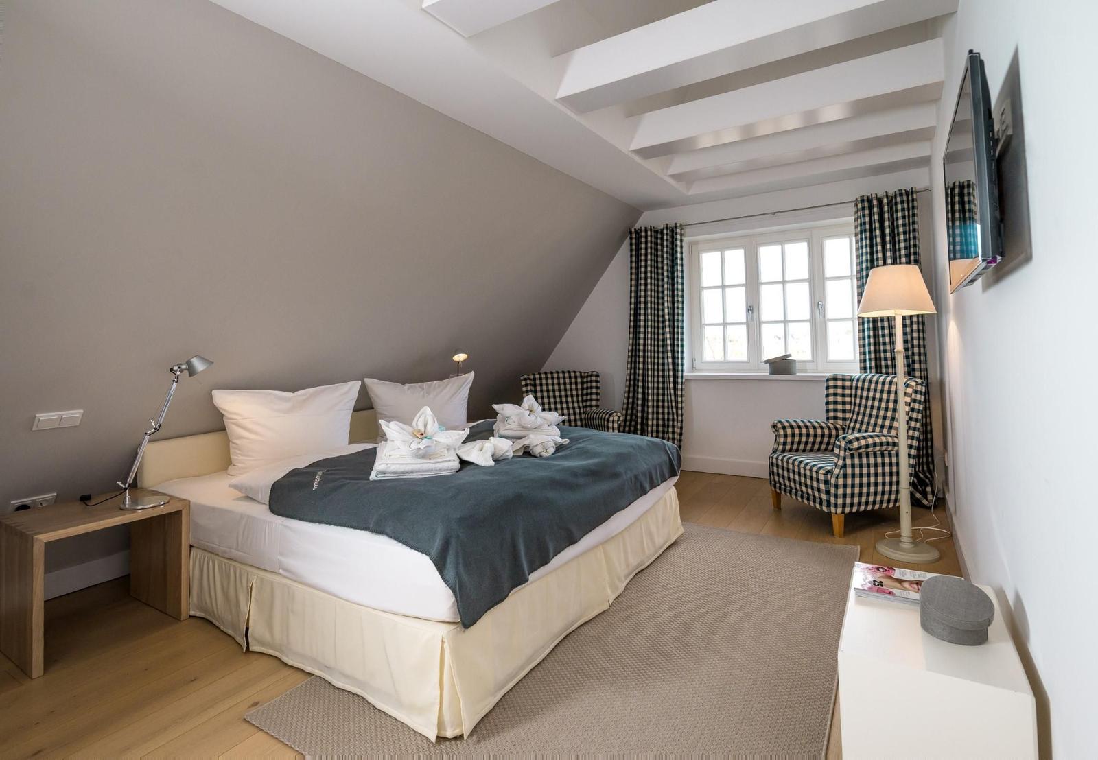 Schlafzimmer mit Doppelbett, zwei Sesseln und Fenster mit Vorhängen.