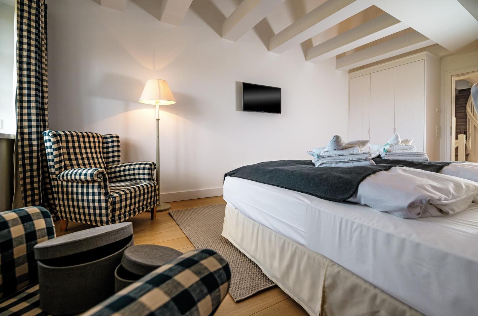 Schlafzimmer mit Bett, Sessel und Fernseher an der Wand.