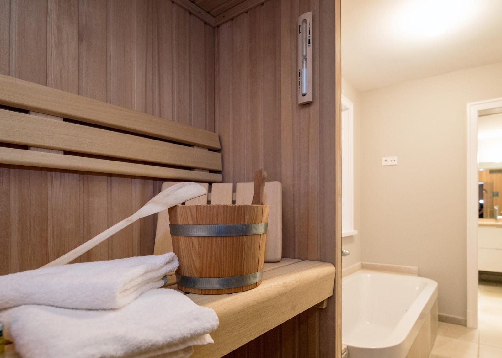 Sauna mit Holzbank, Eimer und Handtuch. Nebenraum mit Badewanne.