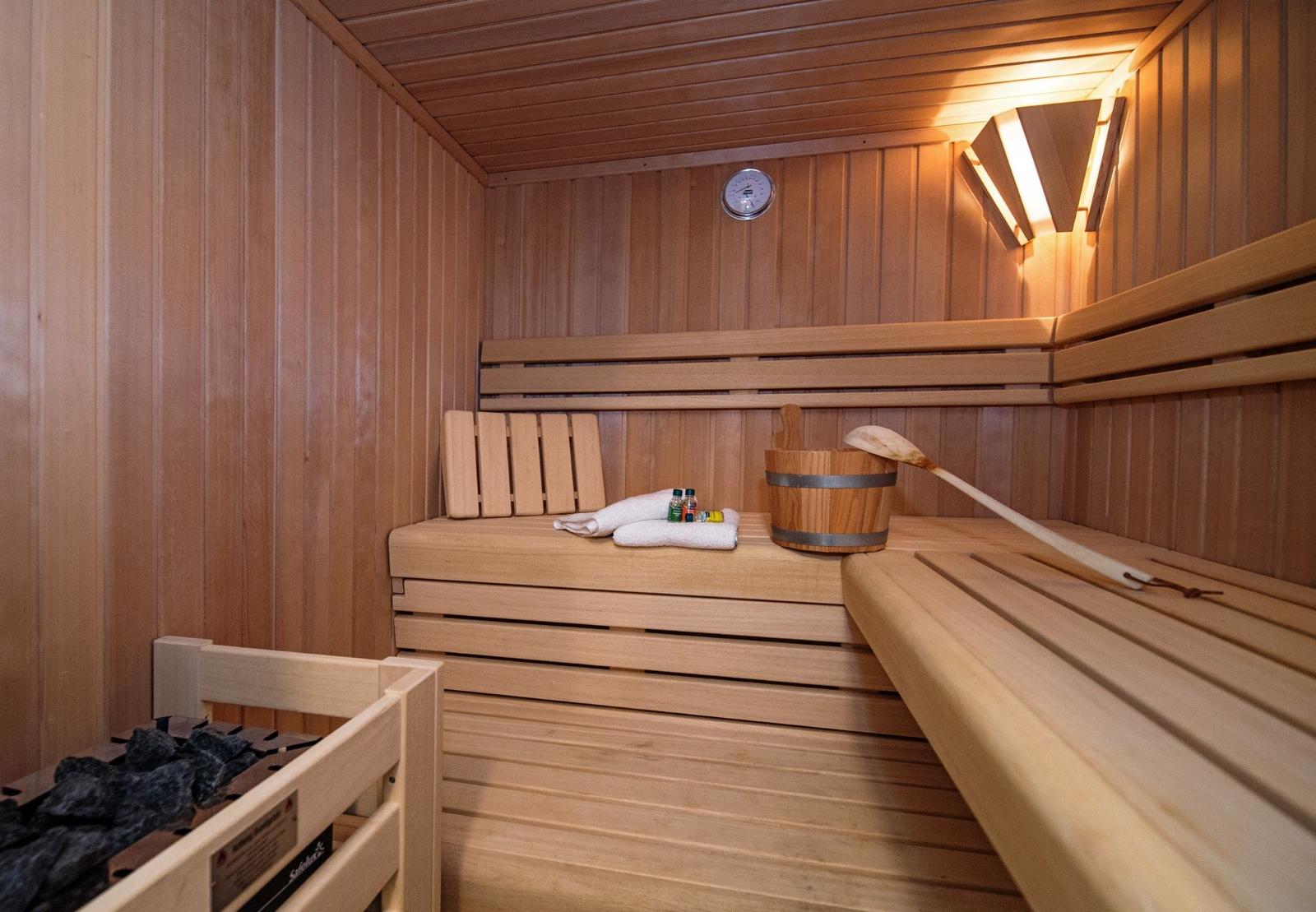 Sauna mit Holzbank, Körbchen und Thermometer an der Wand.