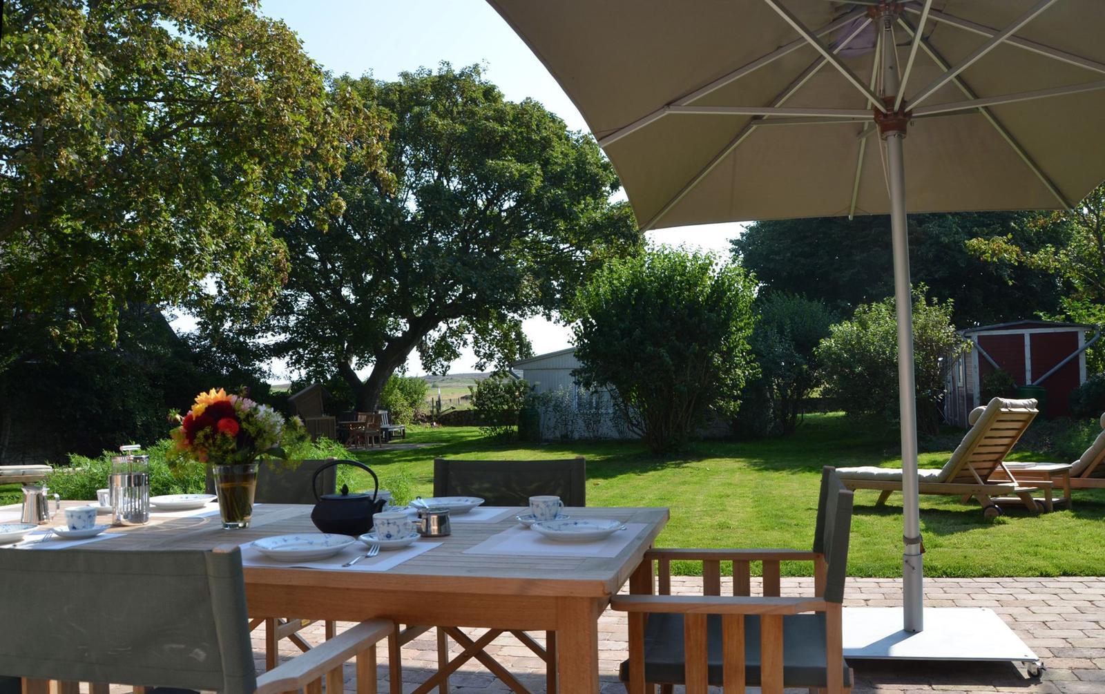 Terrasse mit gedecktem Tisch, Sonnenschirm und Liegestühlen im Garten.