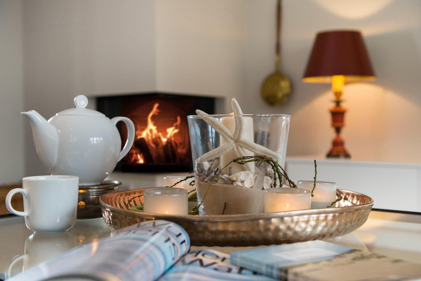 Tisch mit Teekanne, Kerzen und Meeresdekoration vor Kamin