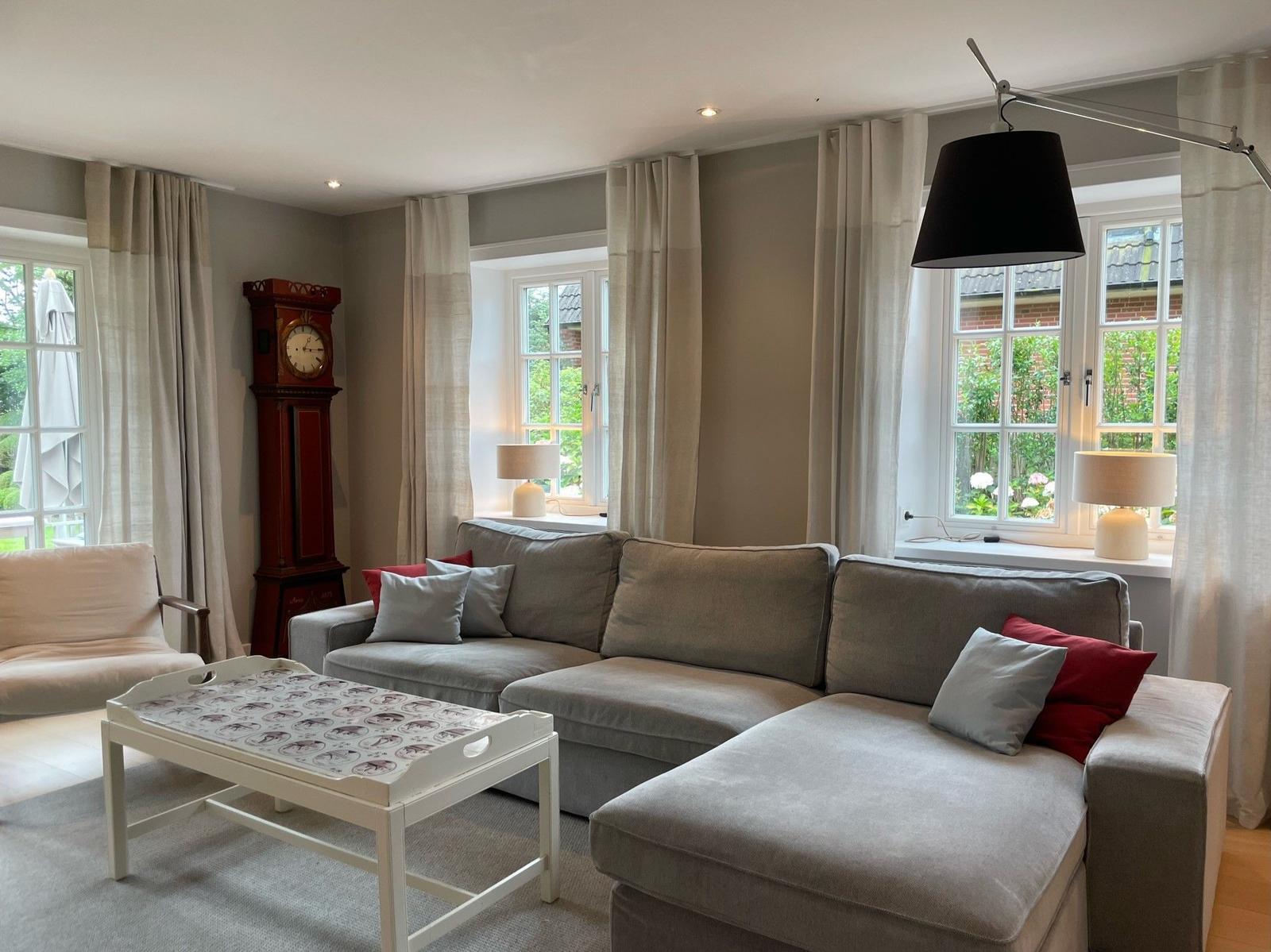 Wohnzimmer mit grauem Sofa, weißem Tisch und hängender Lampe.