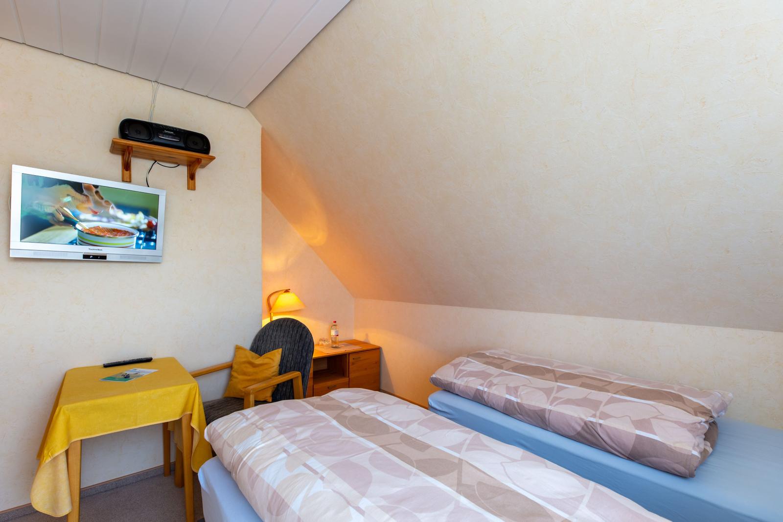 Zimmer mit zwei Betten, Fernseher und Schreibtisch unter schrägem Dach.
