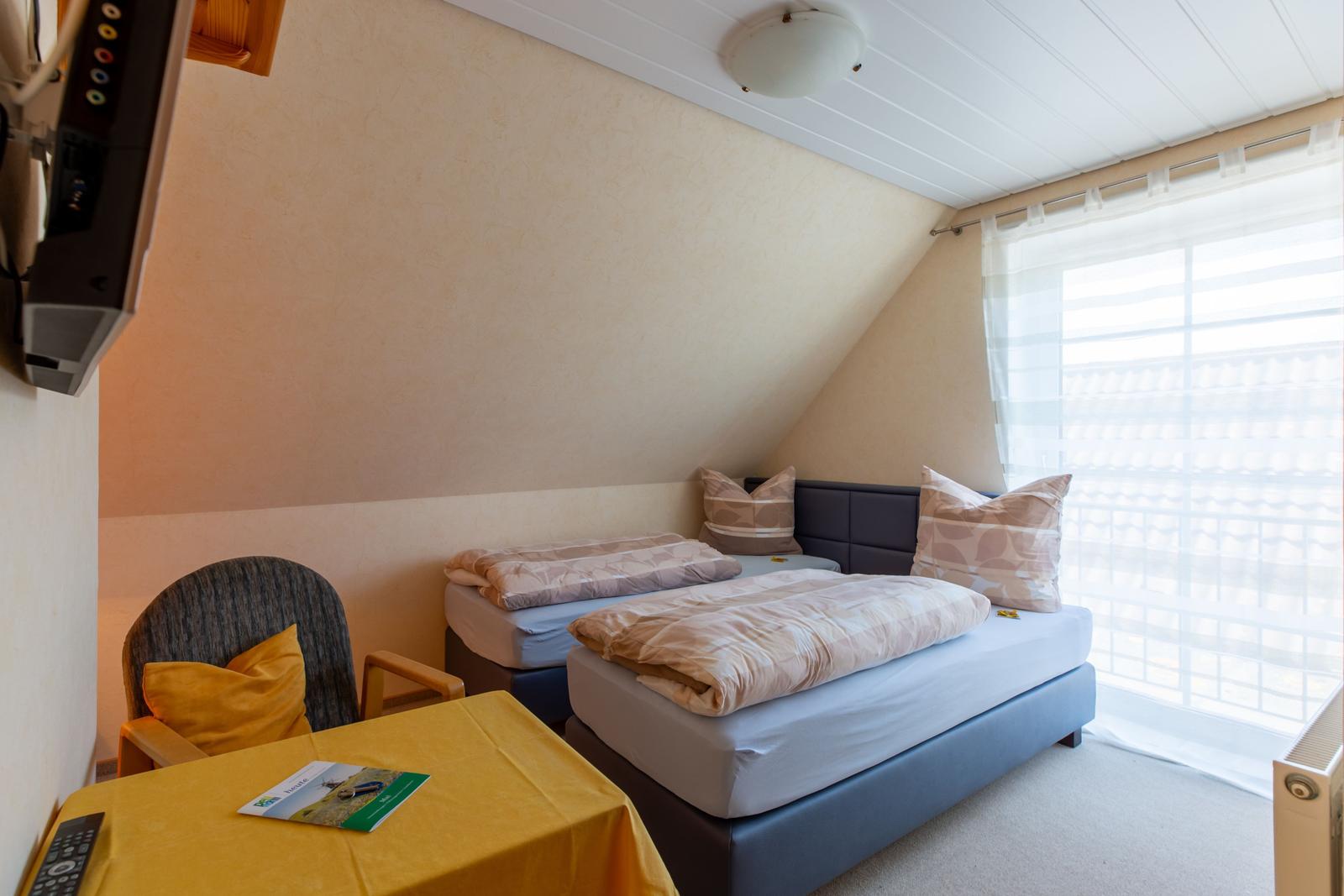 Zimmer mit Doppelbett, Fenster und Schreibtisch mit Stuhl.