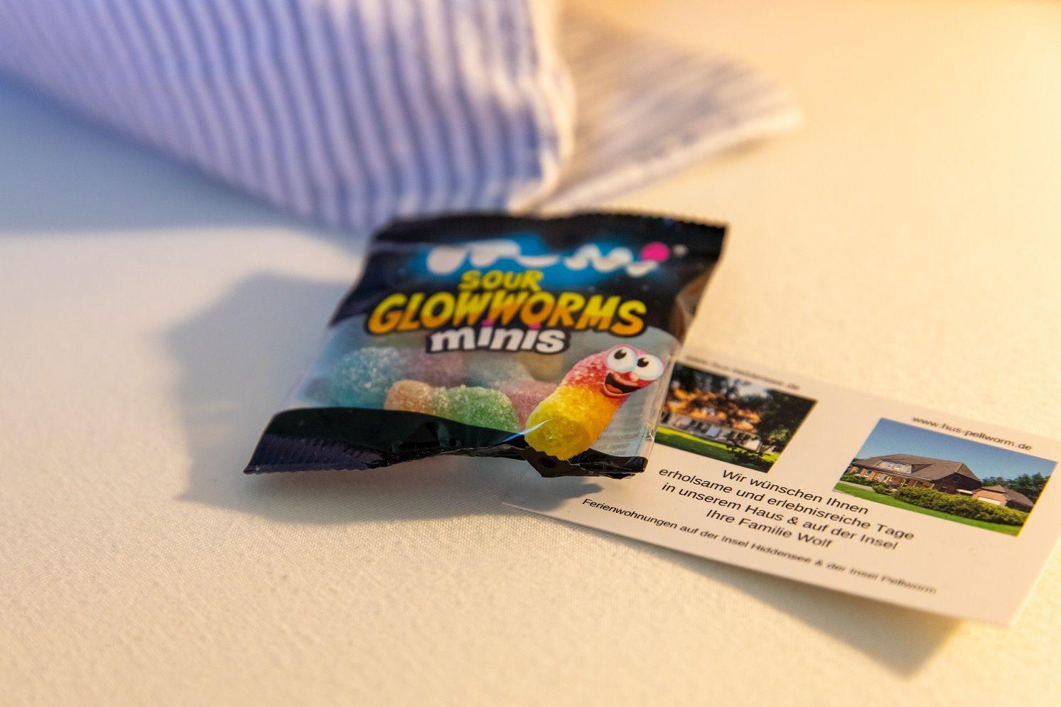 Sour Glowworms Minis und eine Karte mit Ferienhausinformationen liegen auf einer Oberfläche.