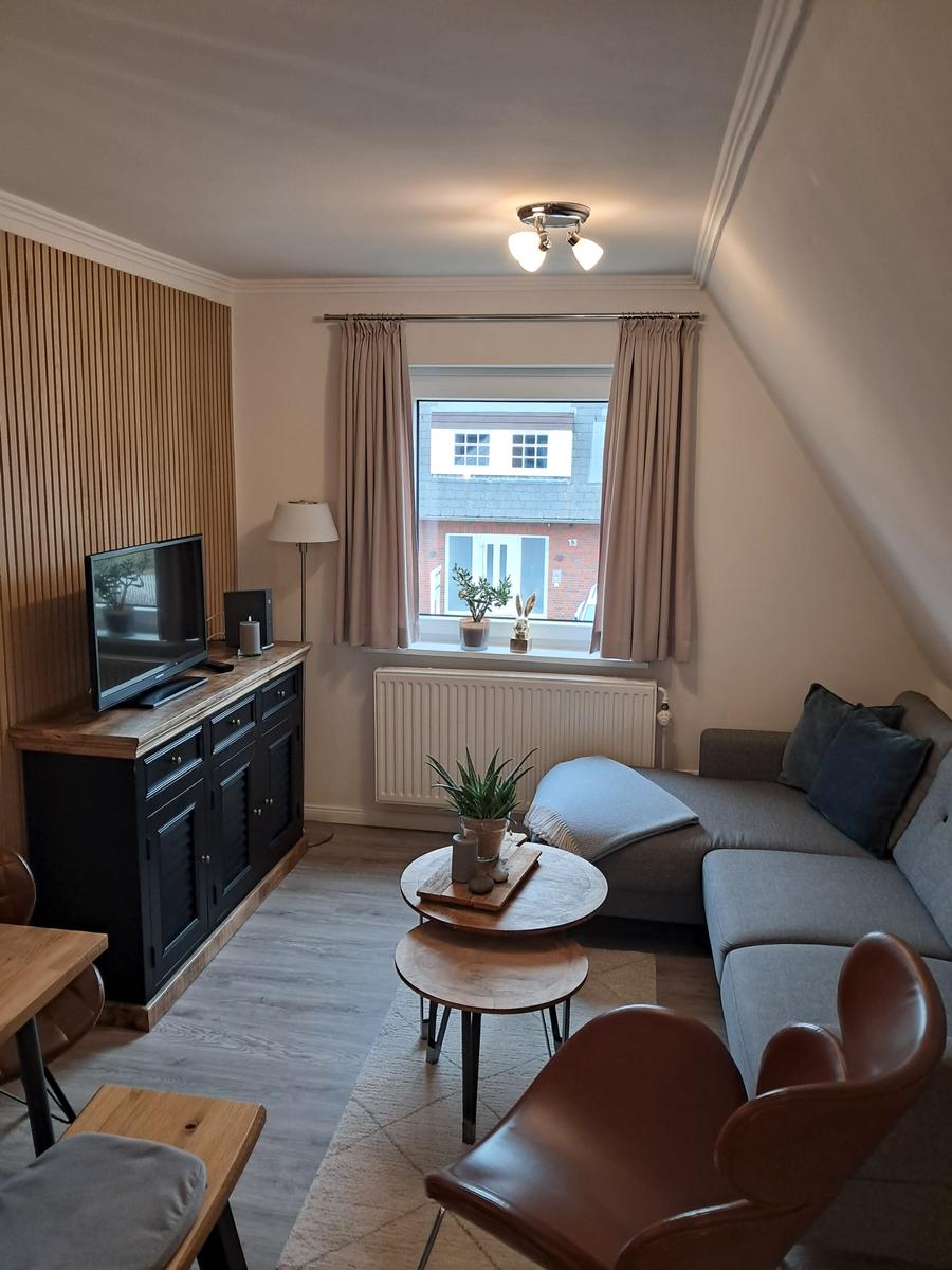 Wohnzimmer mit Sofa, TV und Fenster mit Blick auf Gebäude.