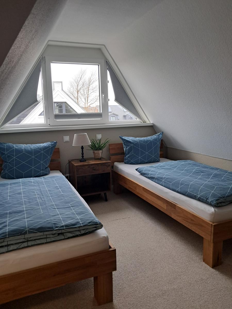 Zwei Einzelbetten mit blauen Bettwäschen unter einem Dachfenster.