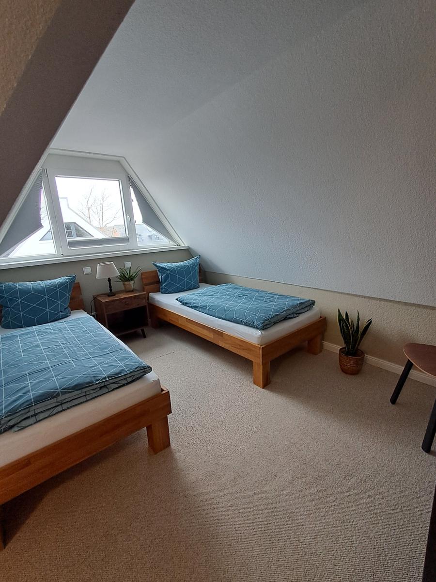 Zwei Einzelbetten mit blauen Bettwäsche unter einem Dachfenster.