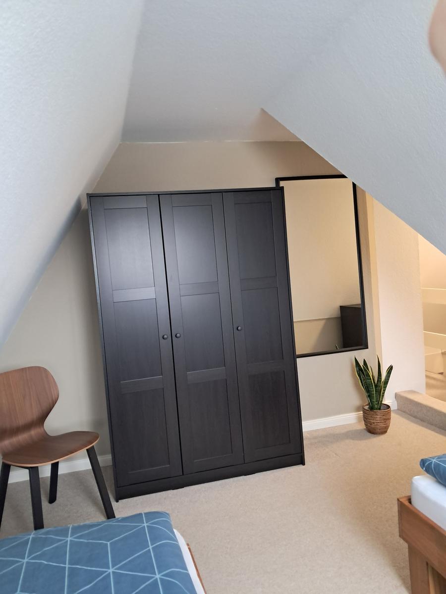 Schlafzimmer mit Kleiderschrank, Stuhl und Pflanze unter schrägem Dach.