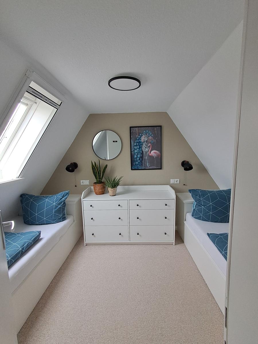 Zimmer mit zwei Schlafcouchen, weißen Schränken und Dachschrägen.