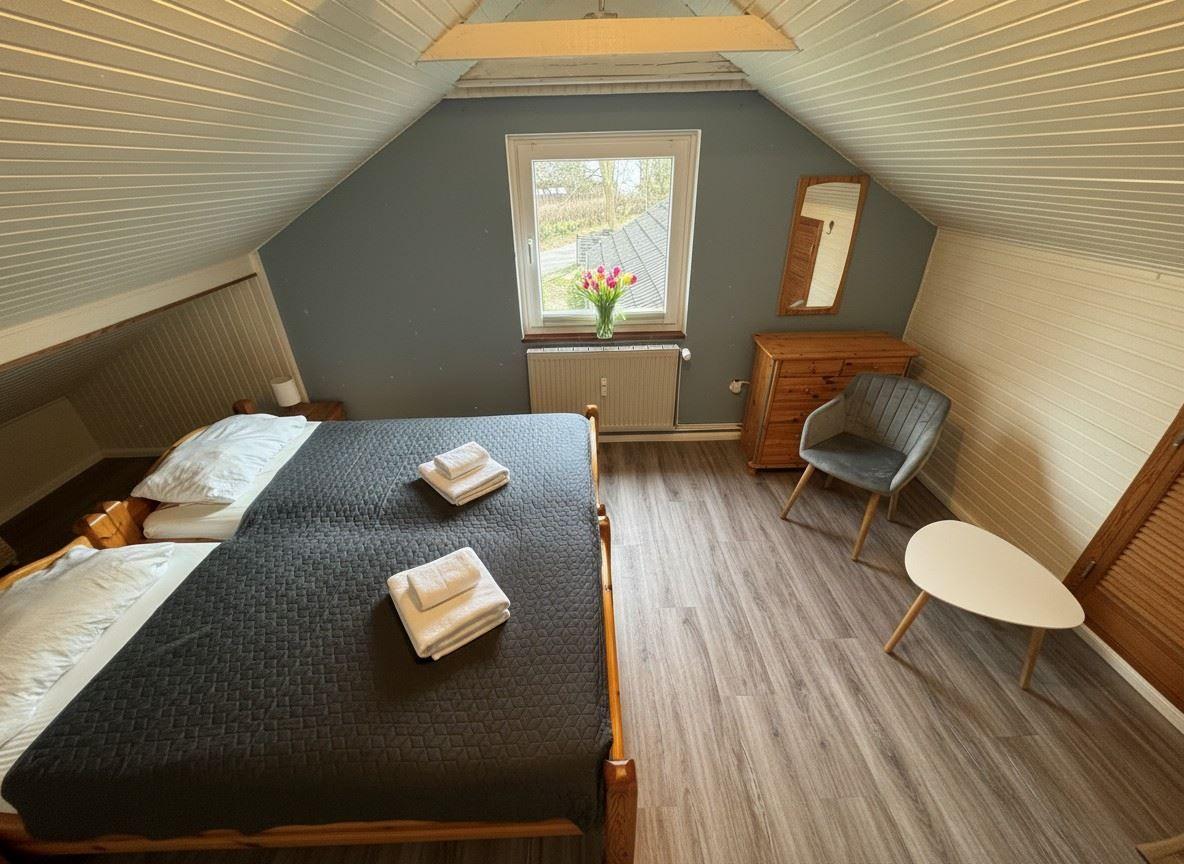 Schlafzimmer mit Dachschräge, Bett, Stuhl und Fenster.