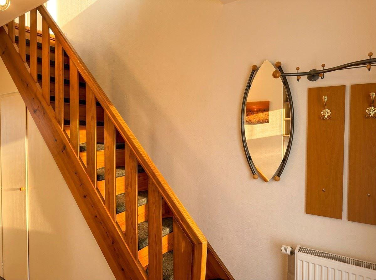 Holztreppe mit Geländer, Wandspiegel und Haken an der Wand.